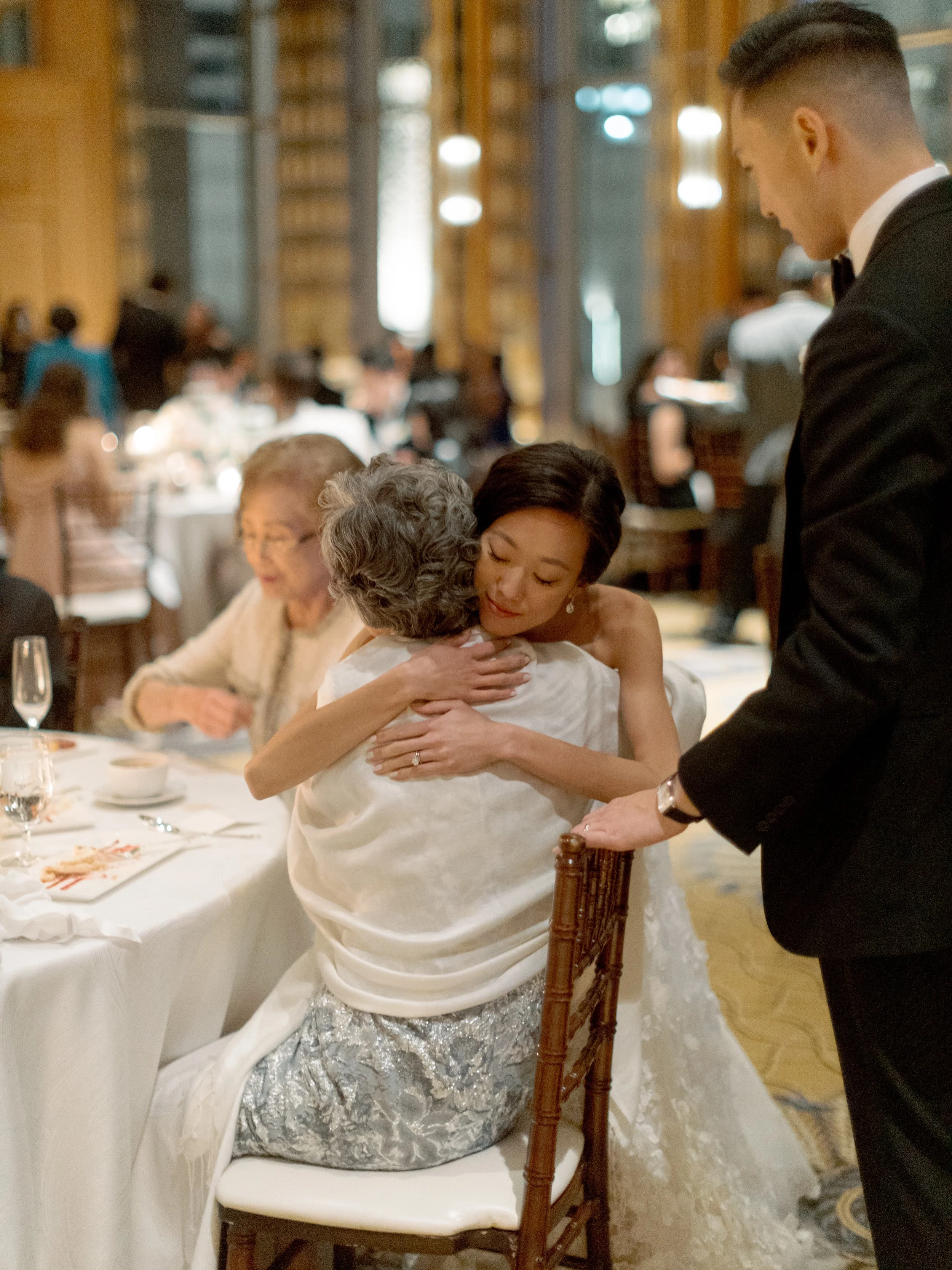 Bride embraces her grandmother seated at the reception table during an emotional moment at The Peninsula Chicago wedding