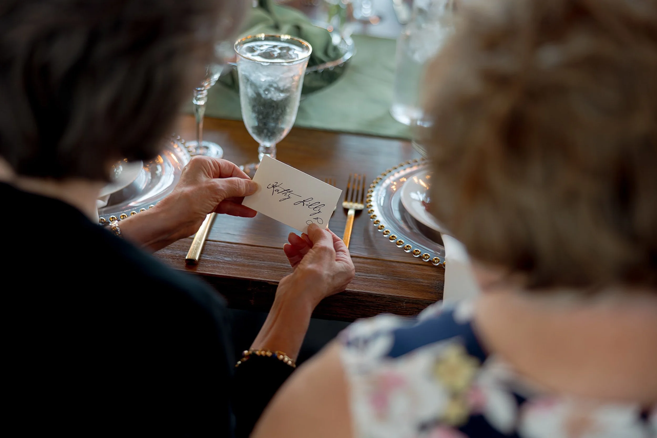 A guest reads her handwritten calligraphy place card over a beaded charger plate — a detail that speaks to the thoughtfulness of the Columbus Park Refectory wedding design