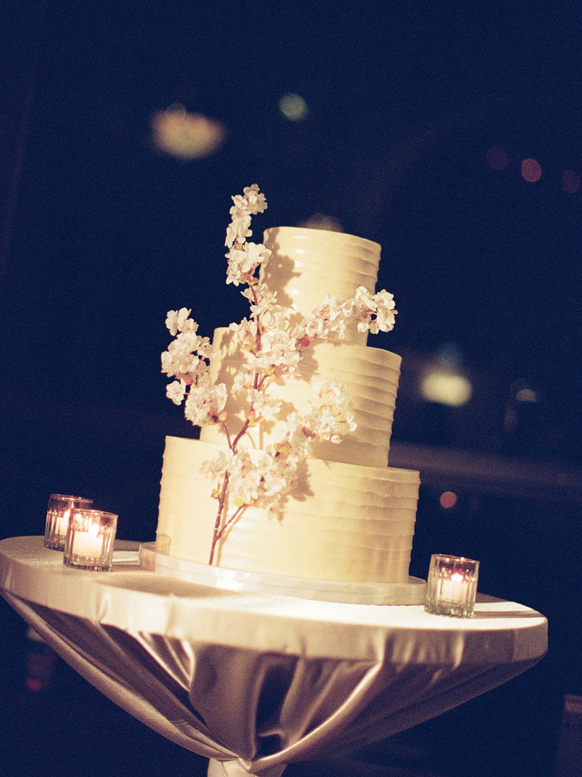 A stunning white tiered wedding cake adorned with a delicate floral spray topper. Shot on film by a Chicago wedding photographer.