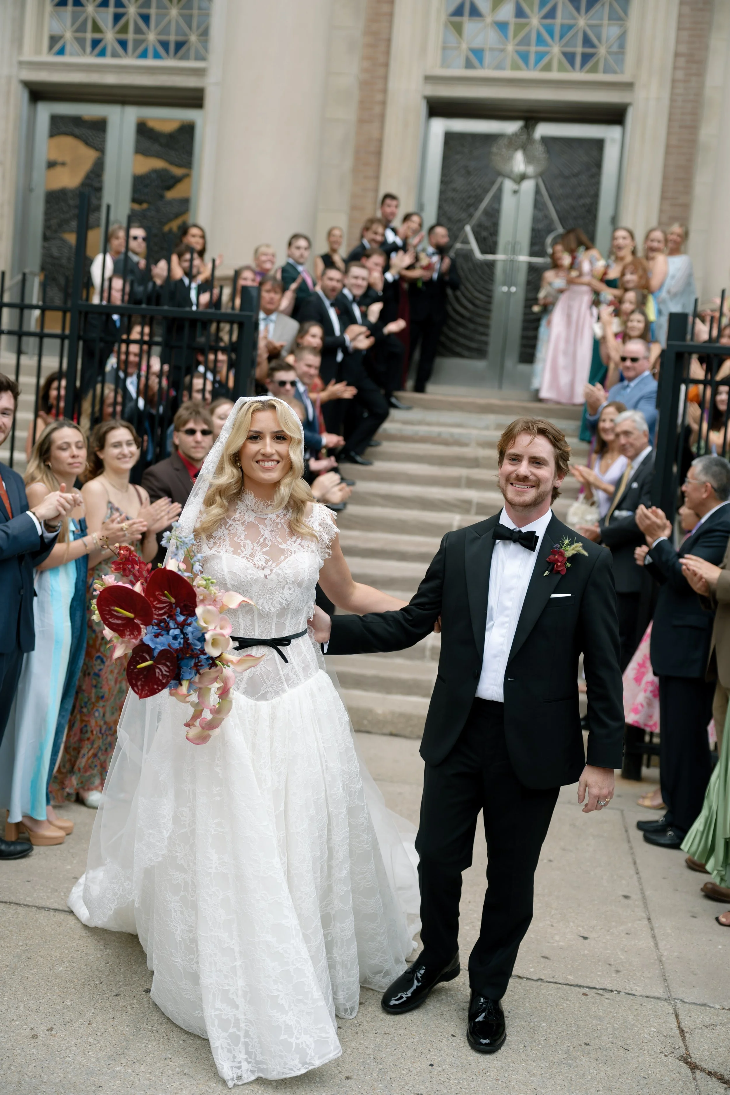 Newlyweds exit the church to cheering guests and confetti on the front steps
