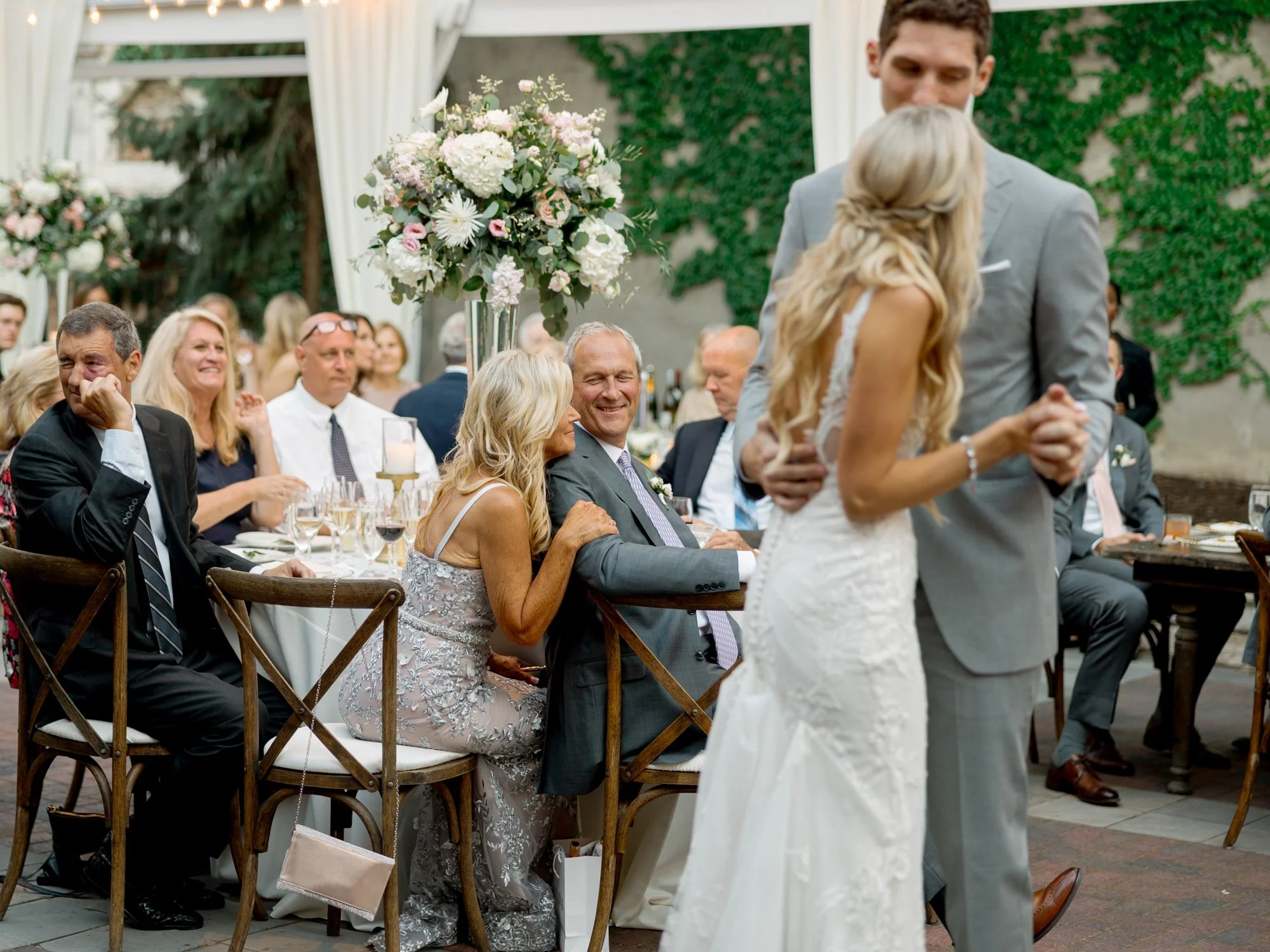 The couple's first dance at the Chicago Illuminating Company, proud parents smiling from candlelit tables adorned with tall floral centerpieces all around them.