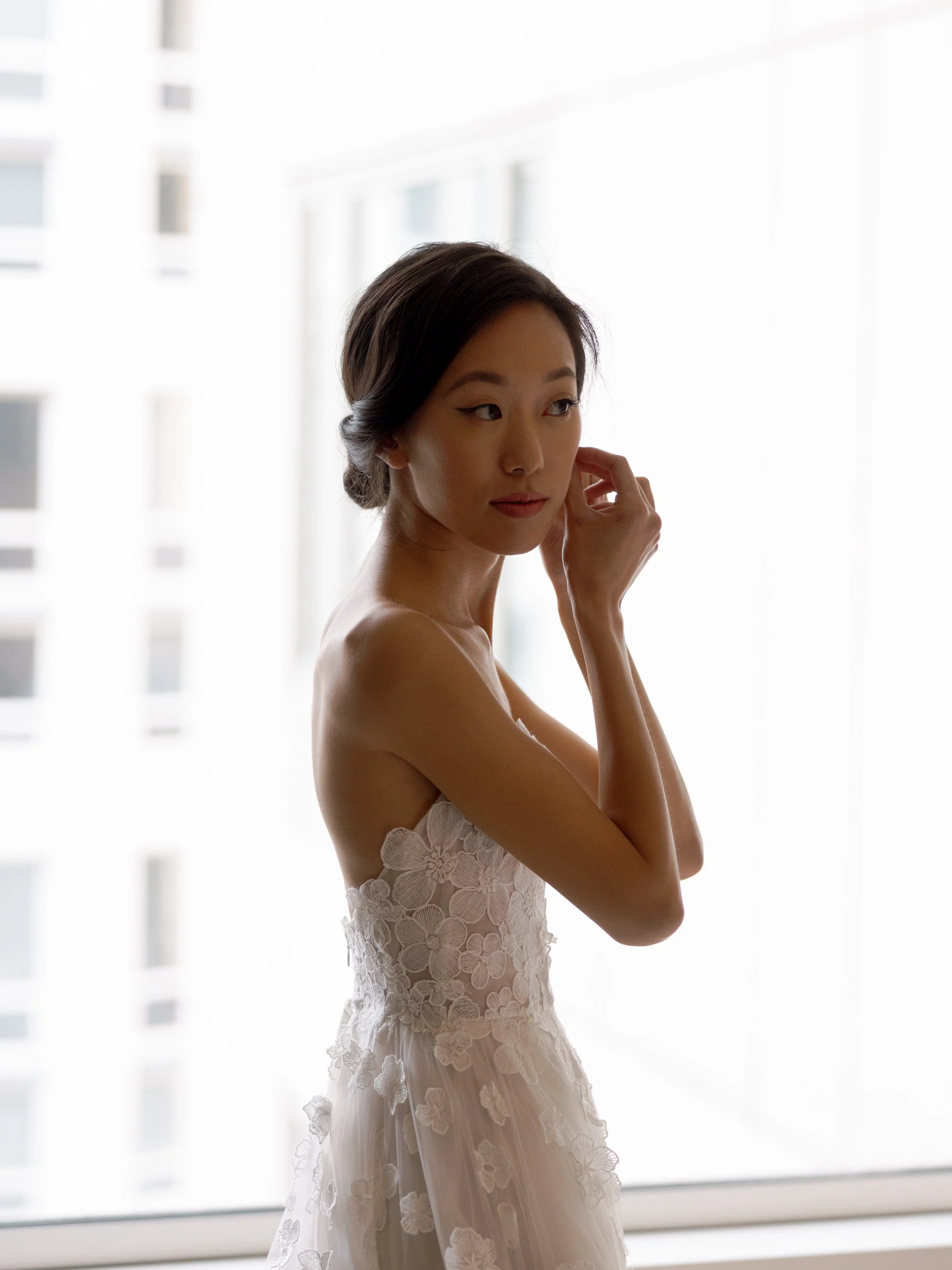 Film bridal portrait of the bride adjusting her earring by window light at The Peninsula Chicago in a floral gown