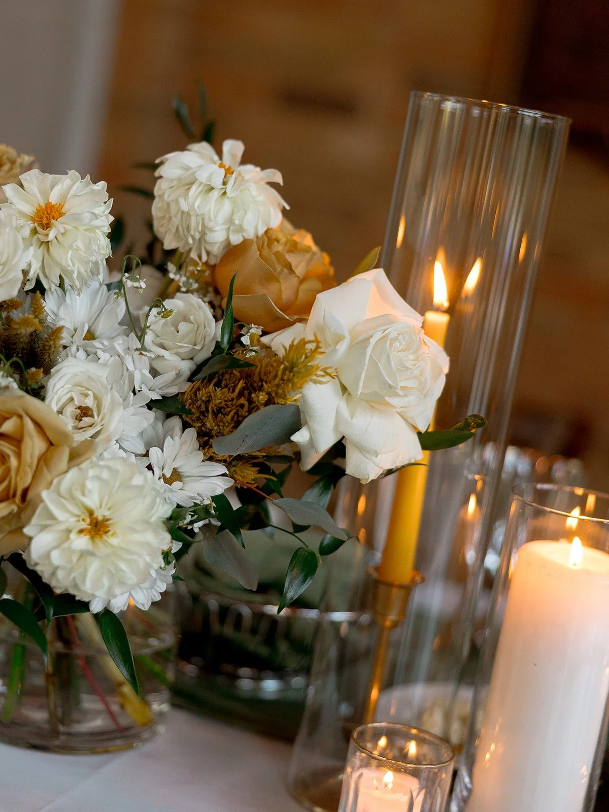 A lush wedding centerpiece of white roses, dahlias, and golden beeswax candles in glass hurricane holders — an intimate table detail from this Columbus Park Refectory reception. Chicago film wedding photographer.