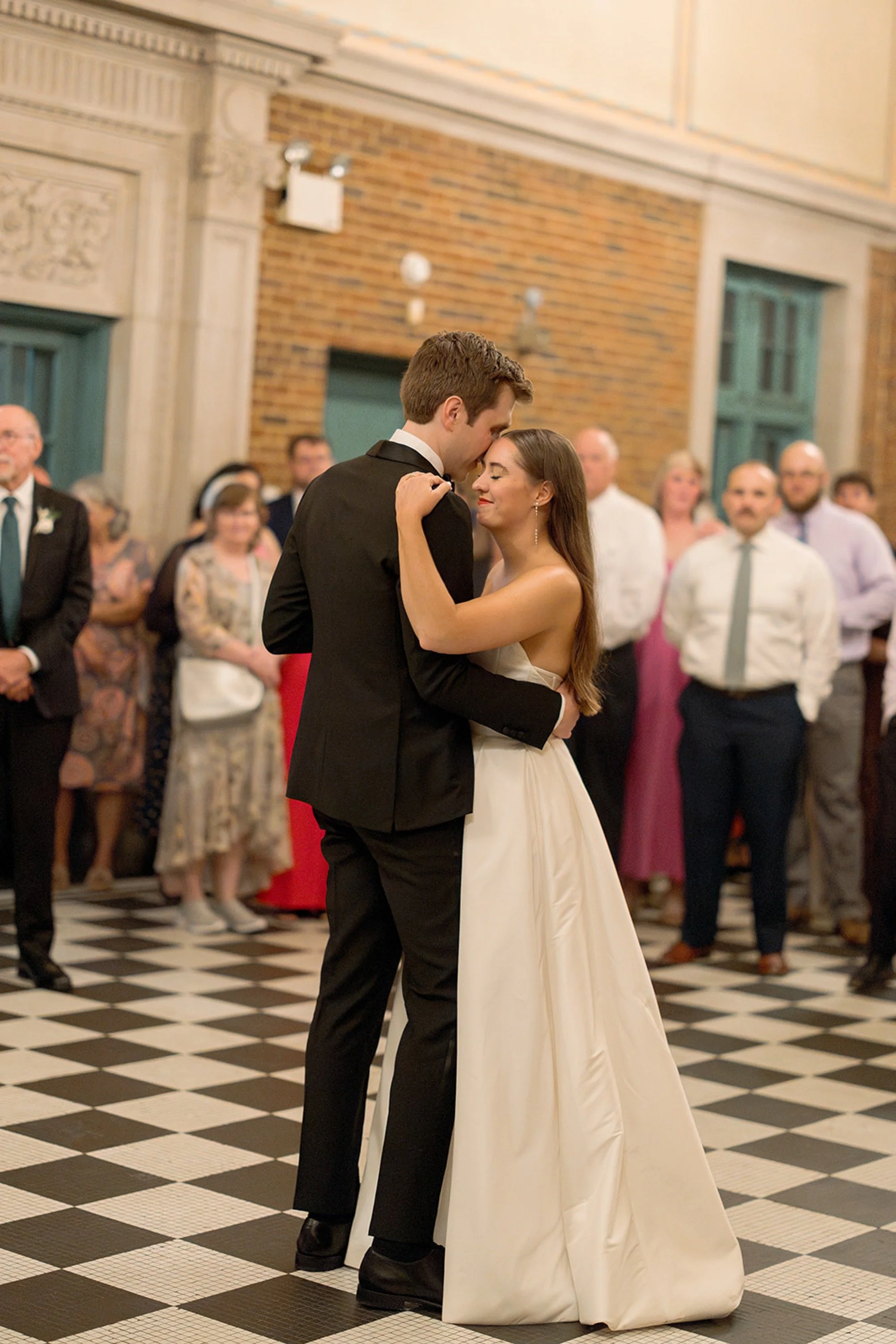 Their first dance — the couple moving slowly together on the iconic black-and-white checkered floor of Columbus Park Refectory, guests encircling them in quiet reverence