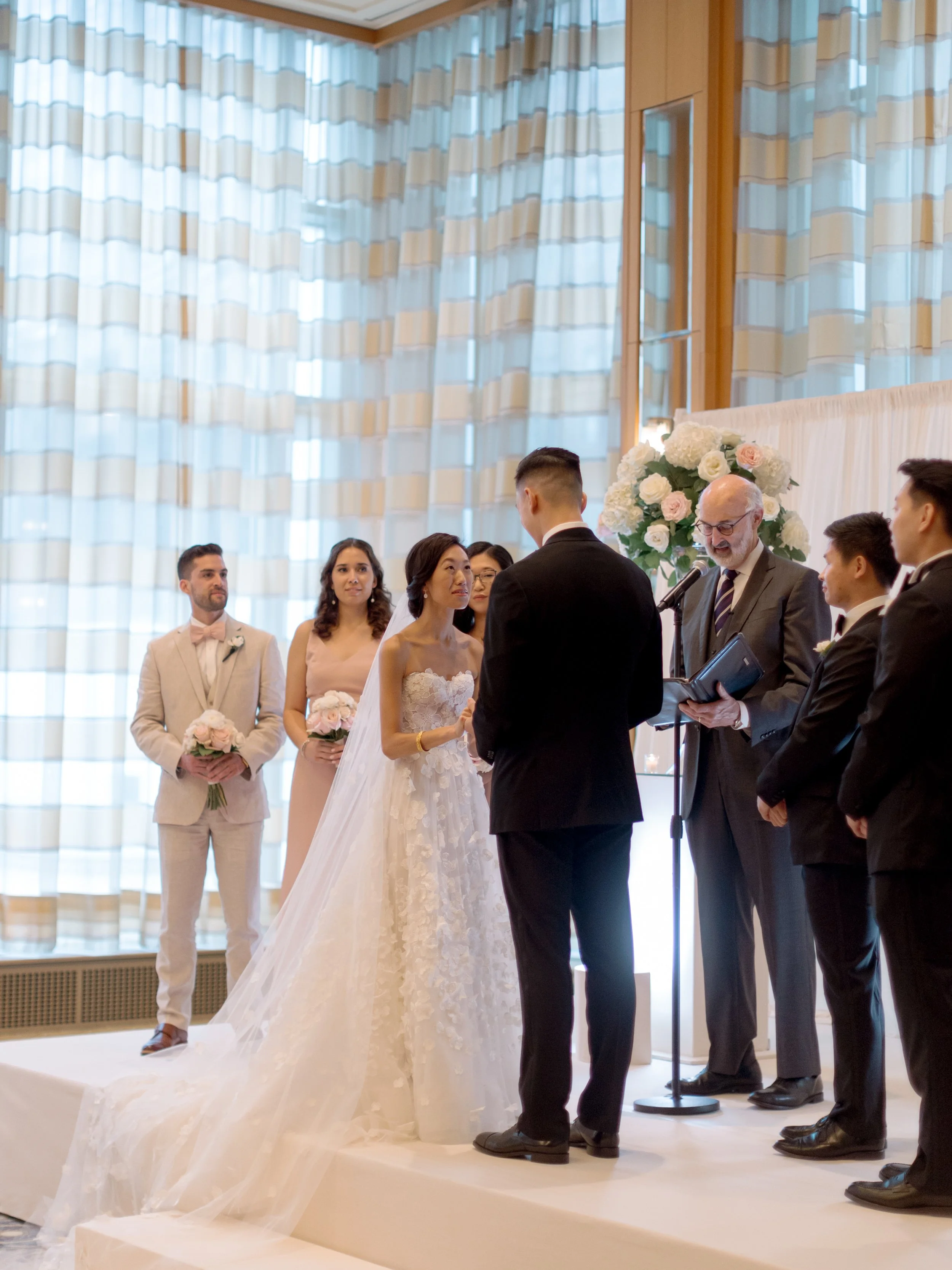 Bride and groom exchanging vows with officiant and wedding party on the ceremony stage at The Peninsula Chicago