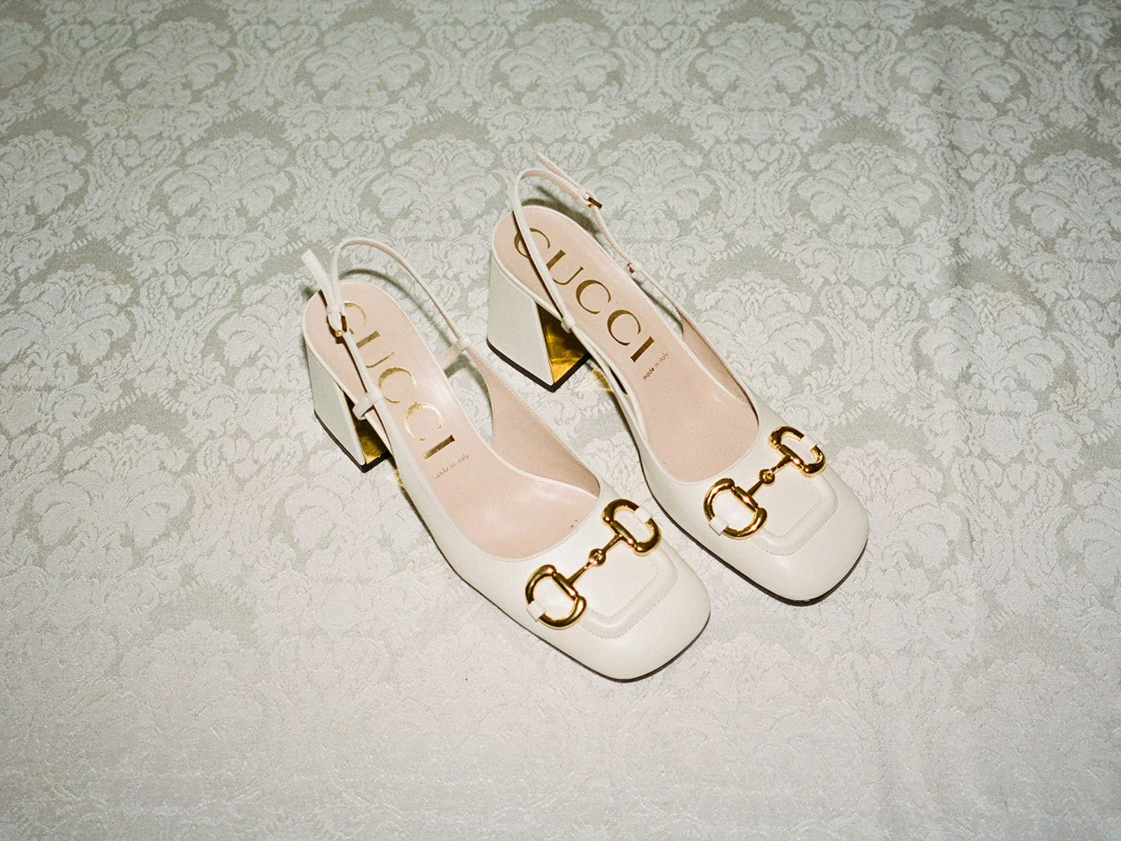 Film detail of ivory Gucci horsebit slingback heels on a lace tablecloth at Columbus Park Refectory in Chicago, photographed by Chicago film wedding photographer Louie Abellera.
