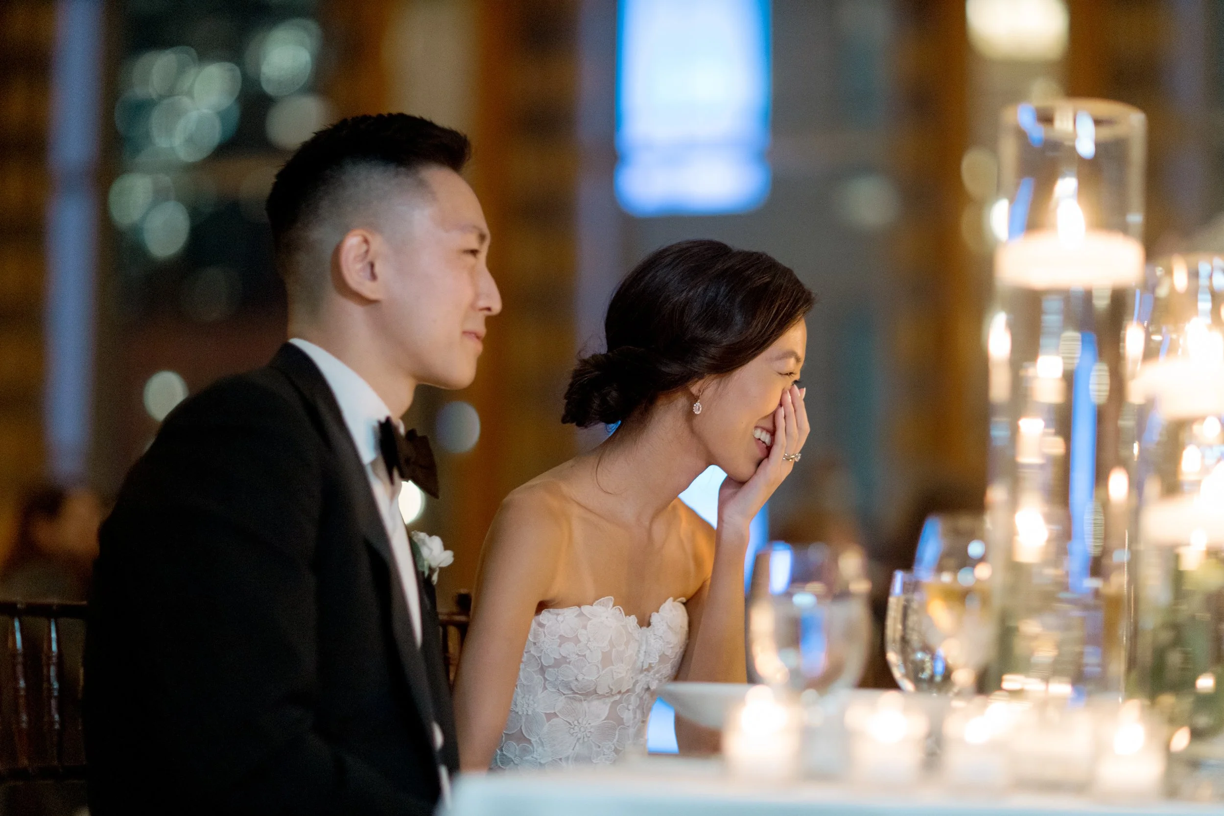 Bride covers her face with emotion beside her groom during a speech at the candlelit Peninsula Chicago reception