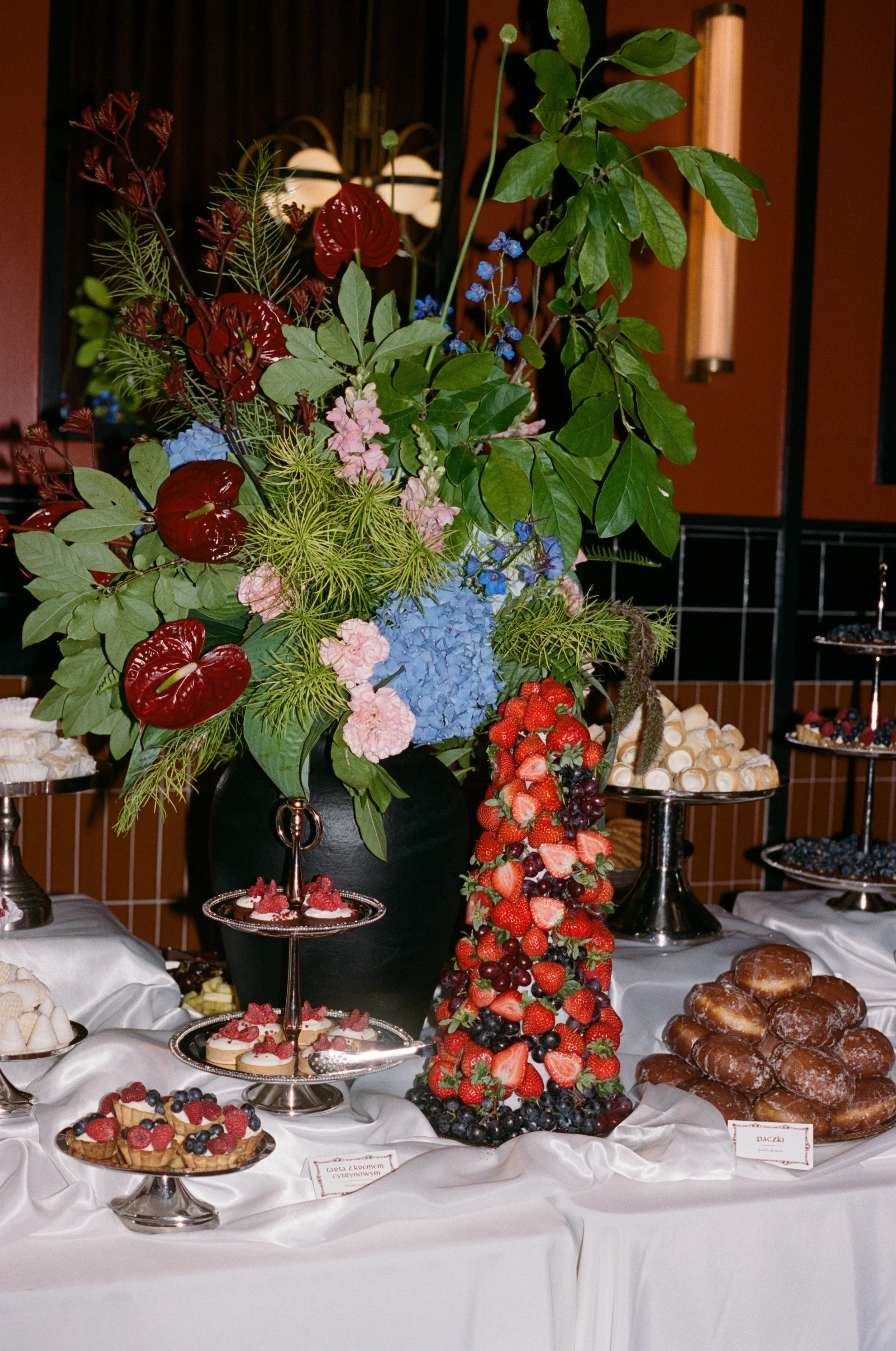 Dessert table styled with a tall floral centerpiece, strawberry tower, and pastries