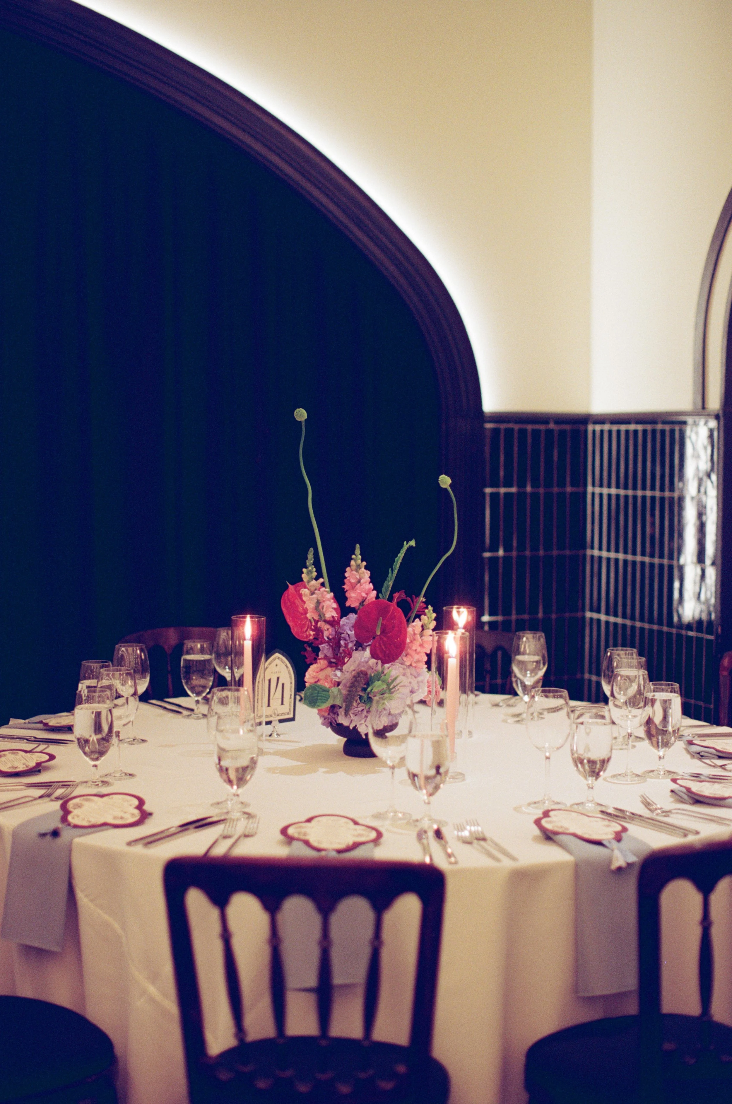 Pink floral centerpiece glows in candlelight at a reception table place setting