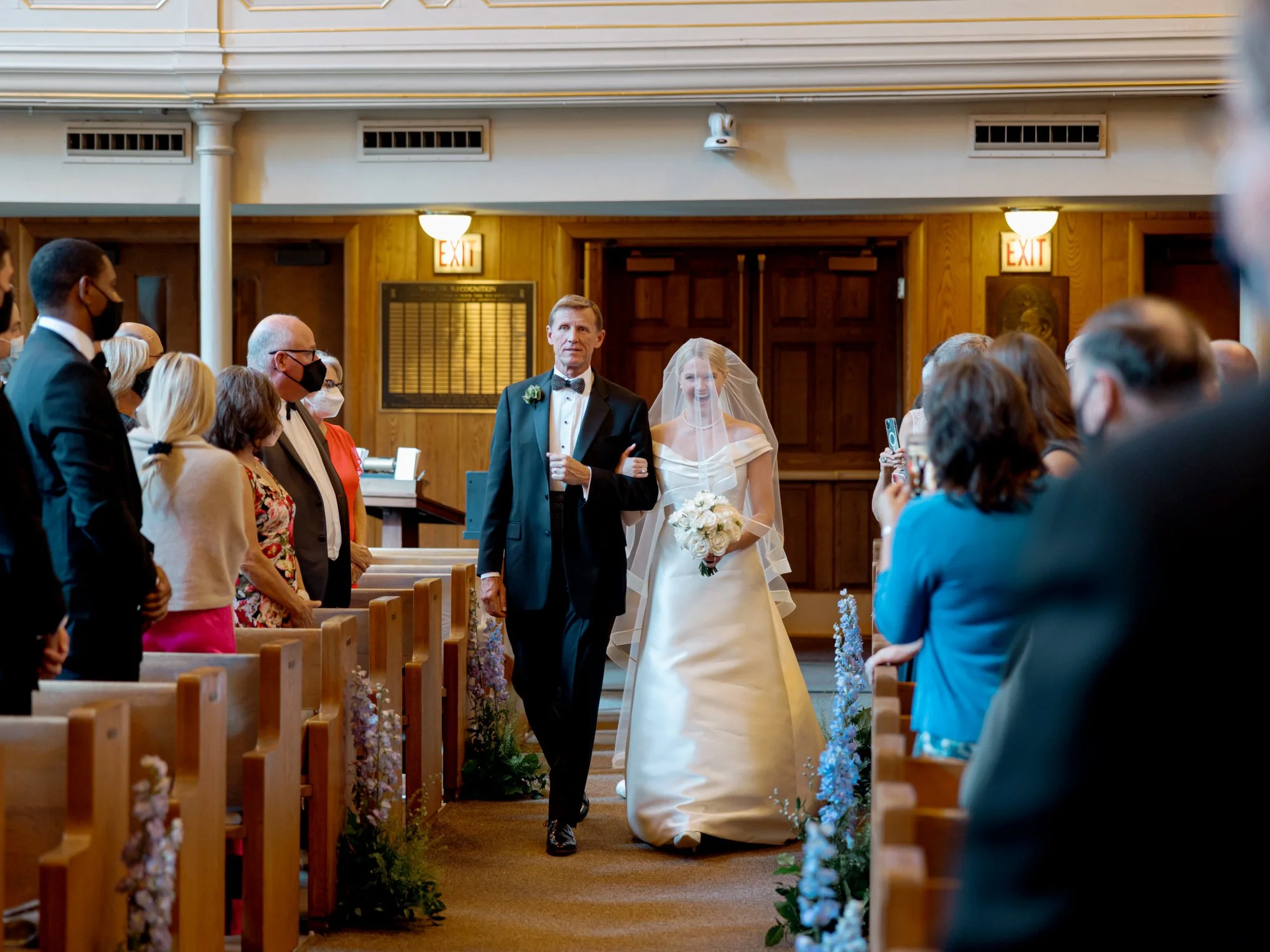The father escorts the bride down the church aisle as the full congregation turns and rises, captured by a Chicago film wedding photographer on 35mm.
