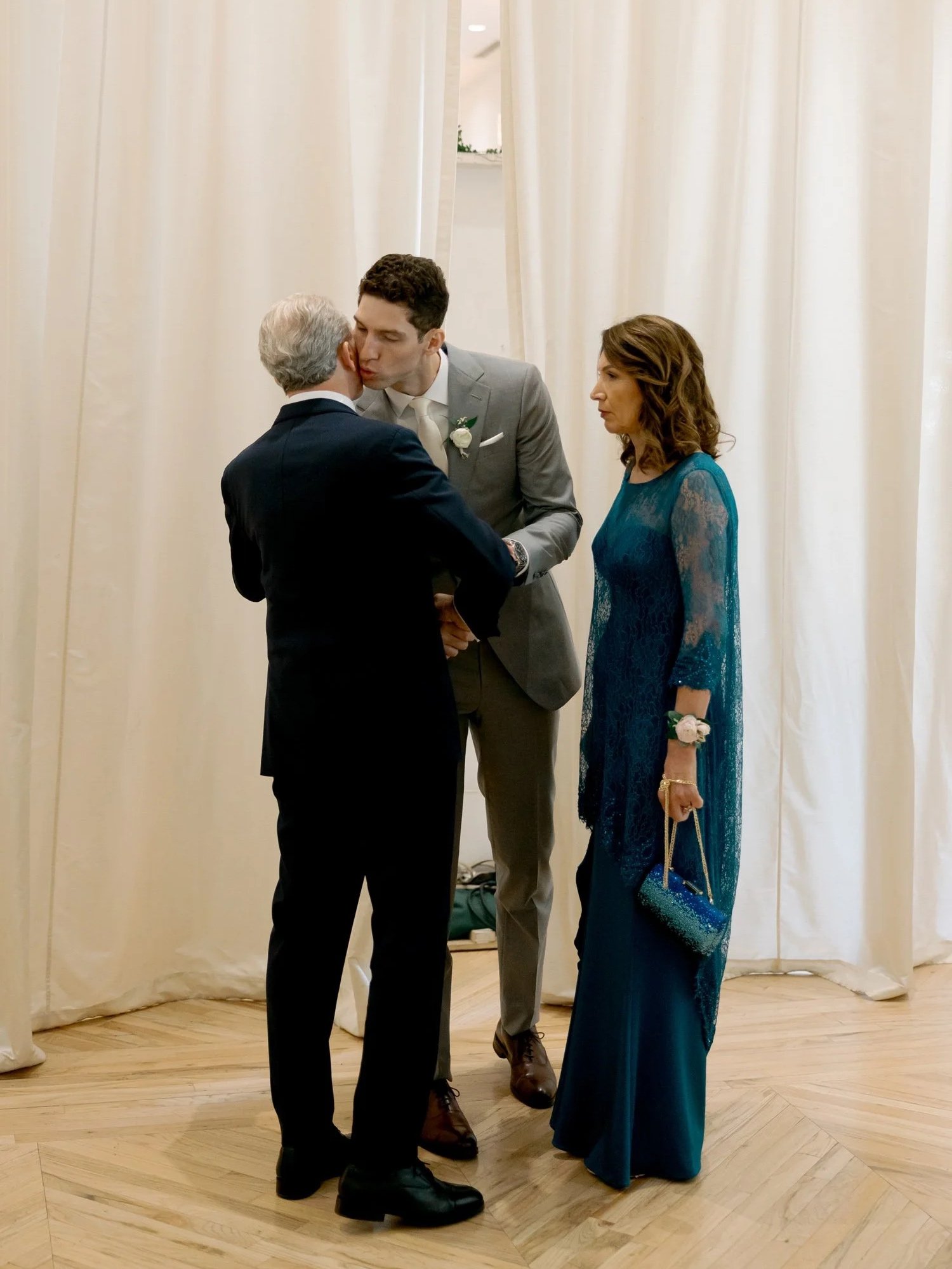 The groom shares a warm pre-ceremony kiss with his father and beams at his mother in the soft-lit interior of the Chicago Illuminating Company.