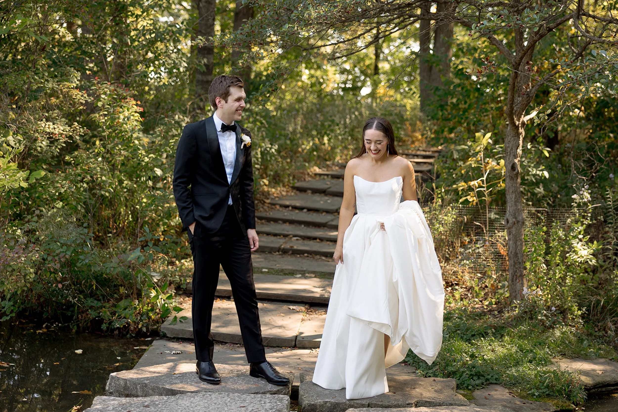 Walking together through the wooded labyrinth of Columbus Park — the couple strolls along a stone bridge path, trees overhead, totally at ease in each other's company