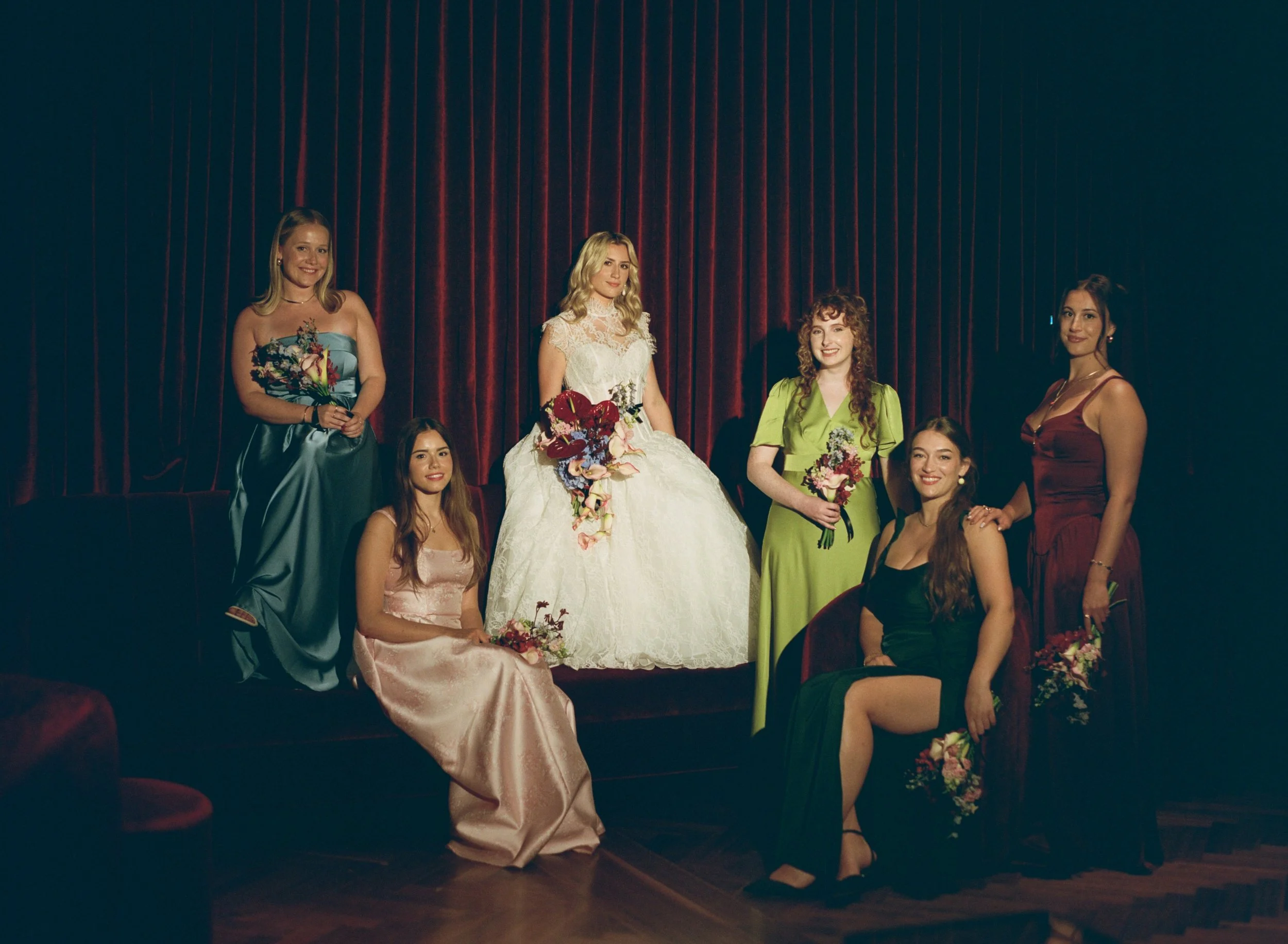Bridesmaids gather around the bride for a group portrait inside The Wellsley's red velvet lounge