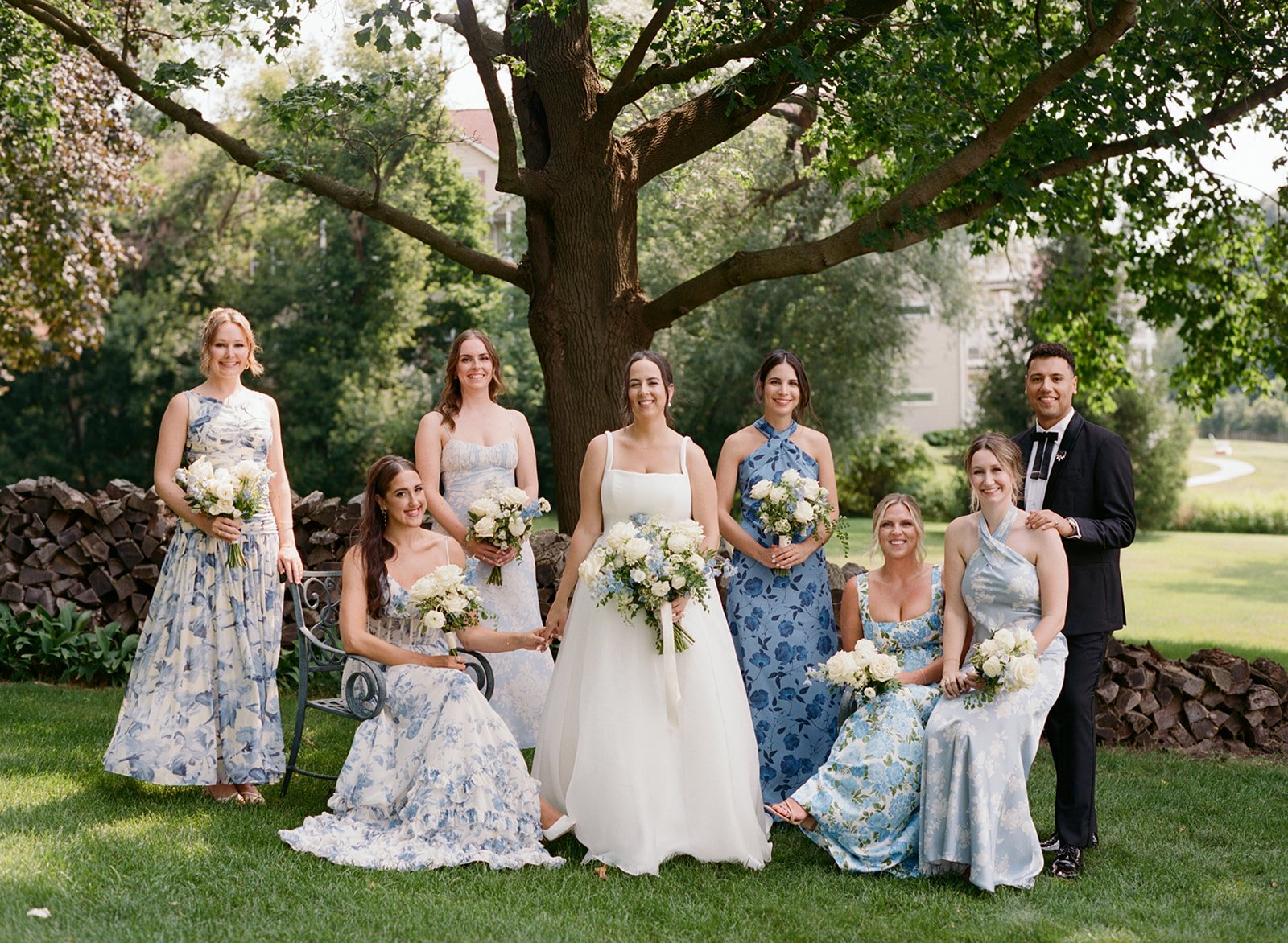 Medium format film portrait of a bride and wedding party in mismatched blue floral dresses on the lawn at Lake Lawn Resort, photographed by Chicago film wedding photographer Louie Abellera.