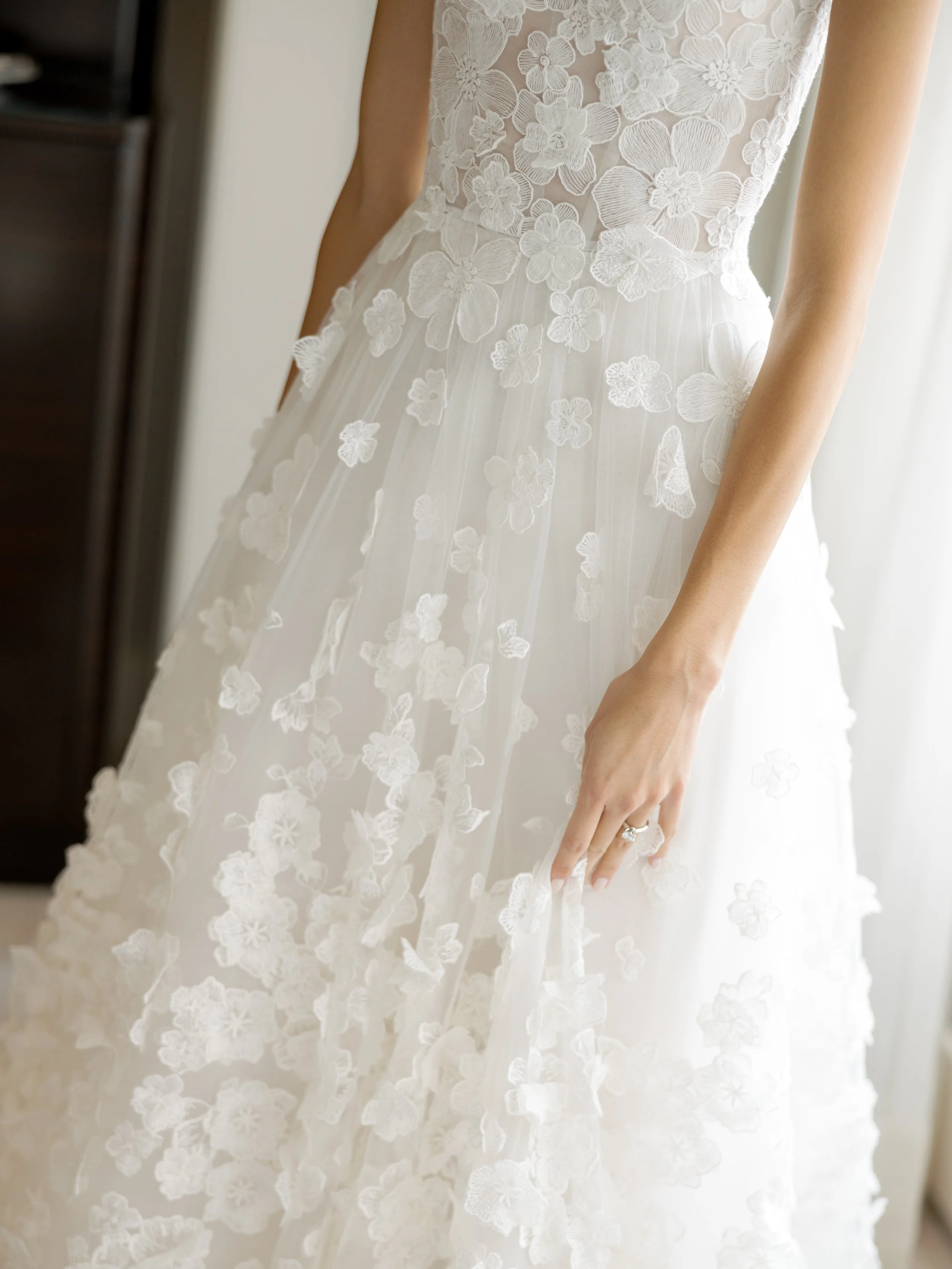Close detail of the brides floral applique wedding gown and her hand with a pave diamond engagement ring