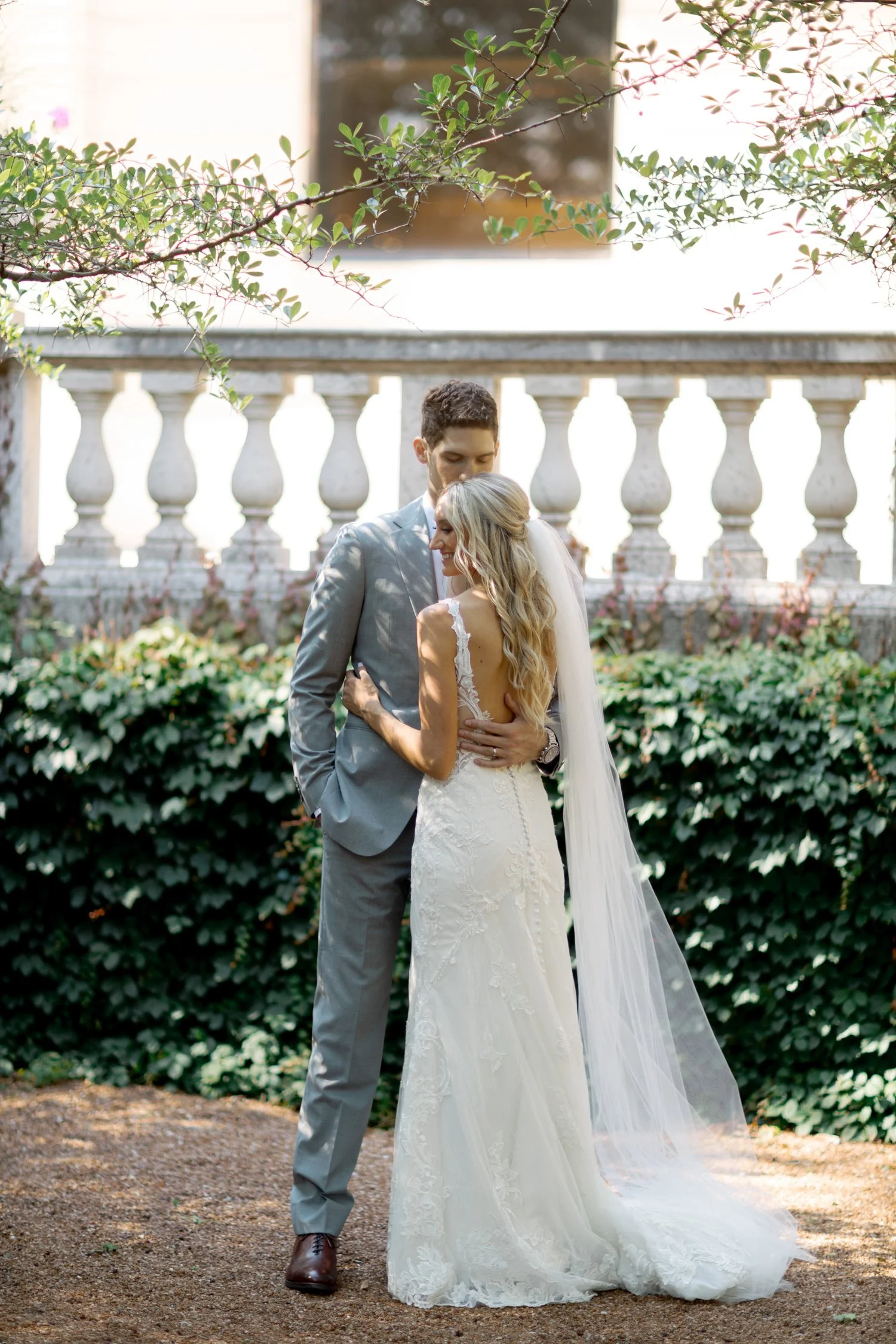 The bride and groom share a quiet moment from behind at the Art Institute South Gardens, the stone balustrade, ivy, and dappled light surrounding them.