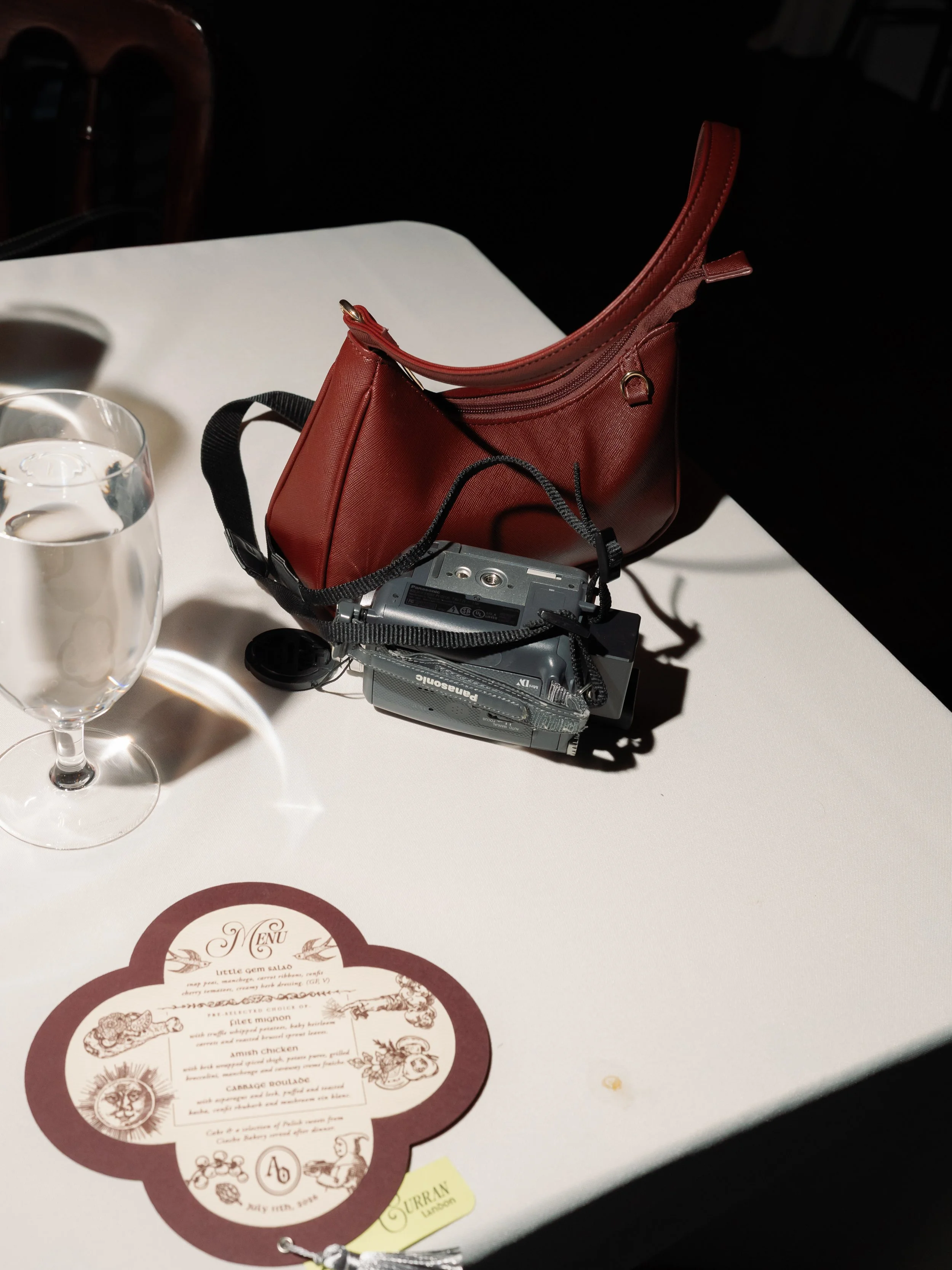 Flat lay of a vintage film camera, red leather clutch, and wedding program on a reception table