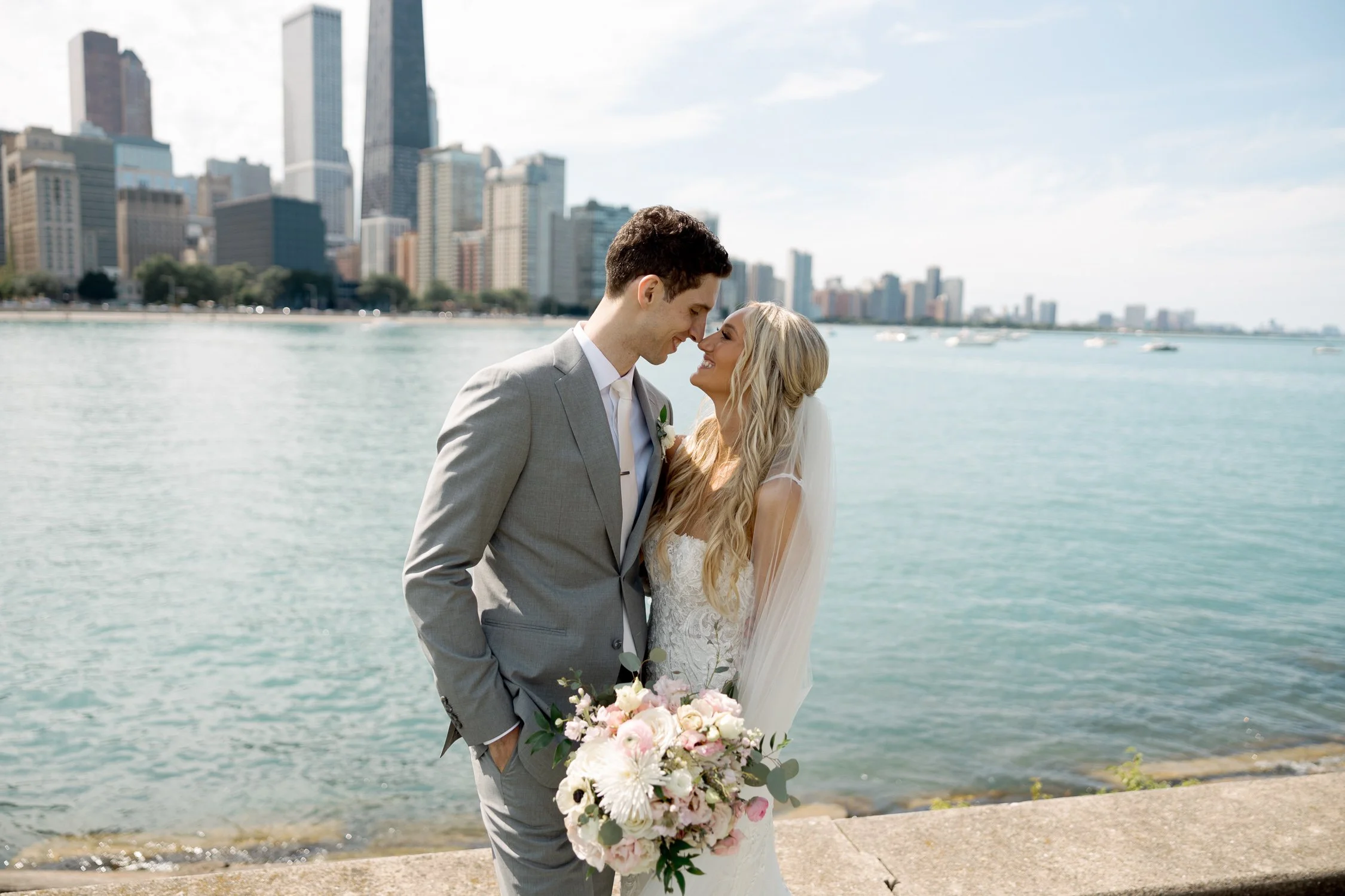The bride and groom lean close at Olive Park, nearly touching foreheads, pink bouquet between them as the Chicago skyline and Lake Michigan stretch behind.