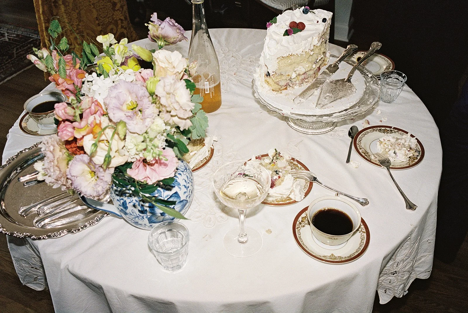 35mm film still of a wedding reception table with floral centerpieces, a partially eaten slice of cake, and a cup of coffee, captured by Chicago film wedding photographer Louie Abellera.