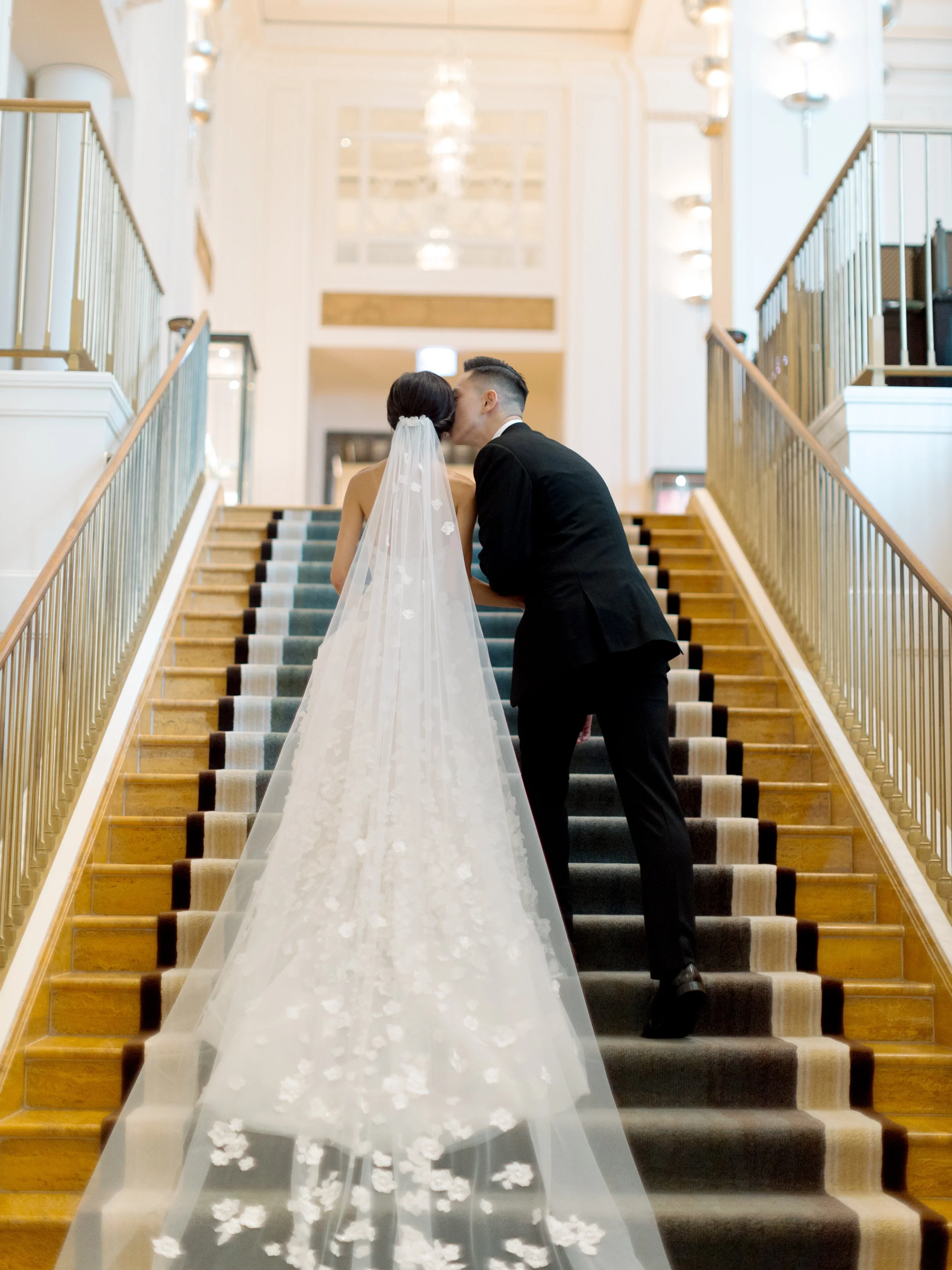 Bride and groom share a kiss on the Peninsula Chicago grand staircase with her floral veil cascading down the steps