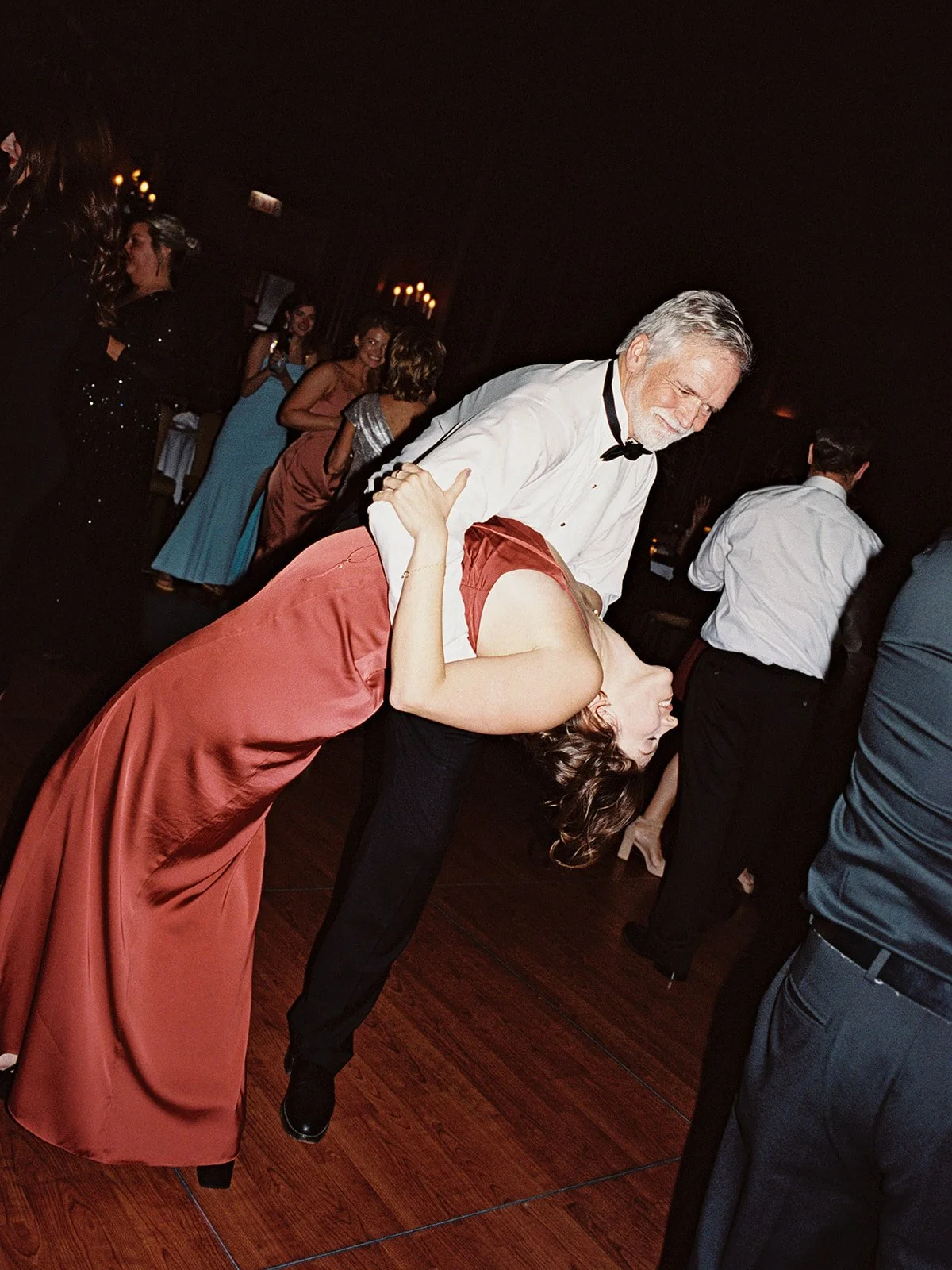 An older guest absolutely owns the University Club Chicago dance floor — dipping his partner in a deep red gown with effortless flair, the whole room dancing behind them. One of those candid film frames that makes a gallery
