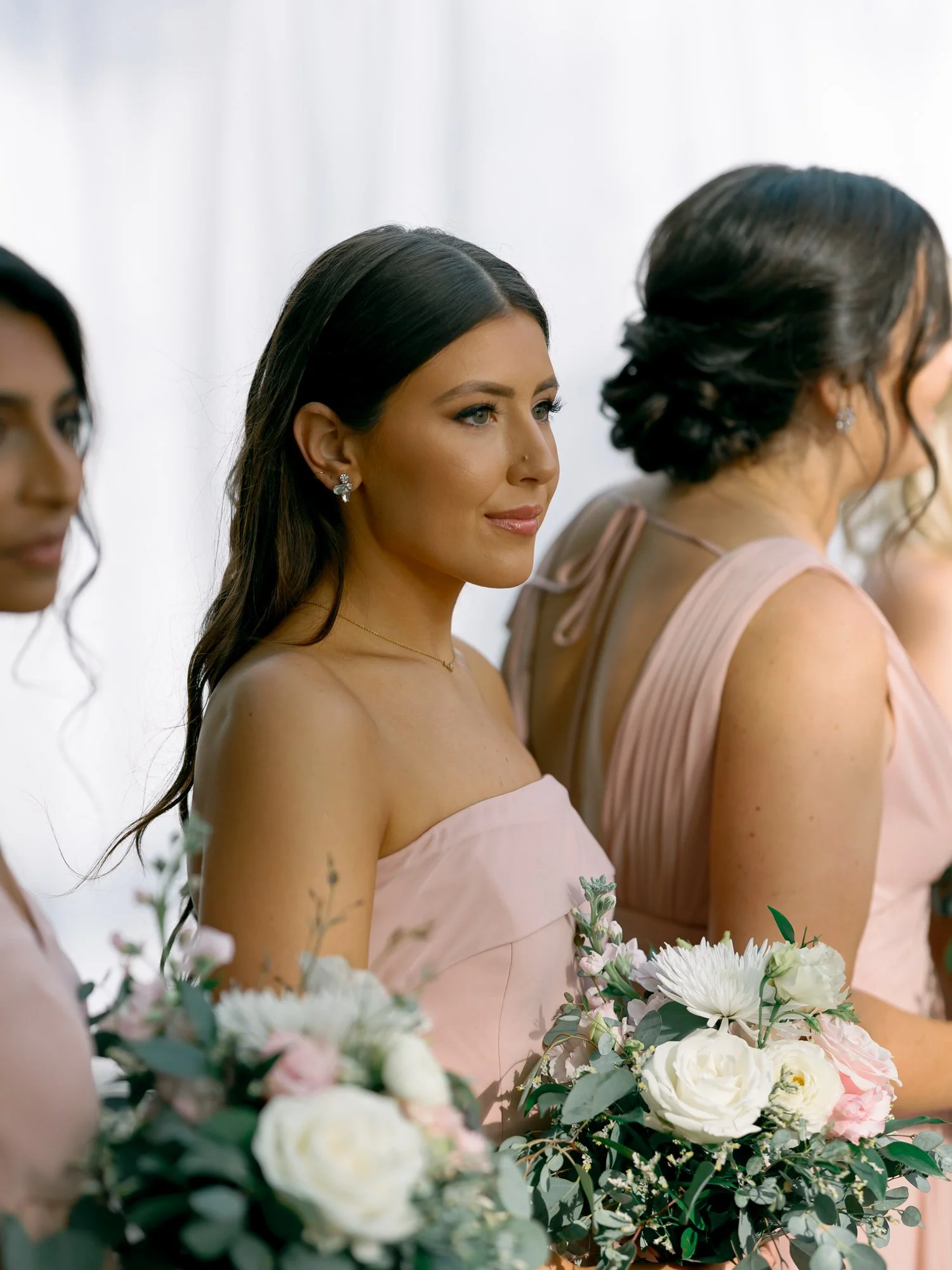 A stunning close-up of a bridesmaid in blush, dark hair swept back and white bouquet in hand, during the ceremony at the Chicago Illuminating Company.