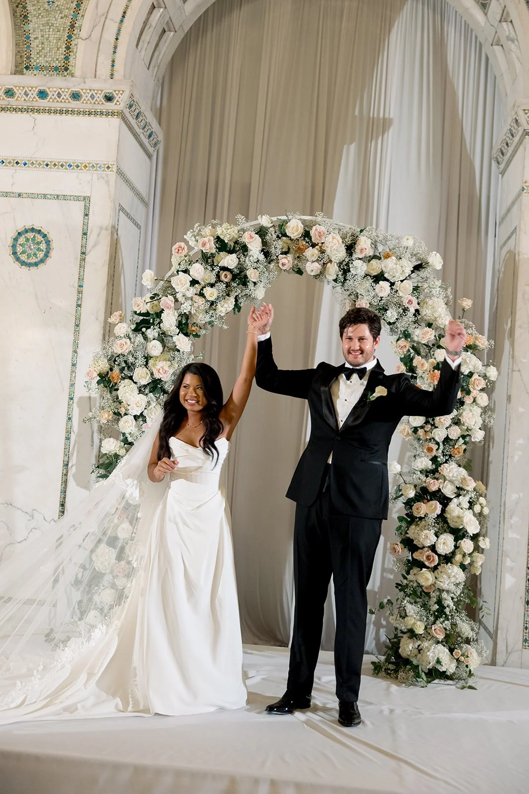 Sarah with her arm raised triumphantly as she and Brennan walk away from the floral arch after their ceremony. Shot on film by a Chicago film wedding photographer.