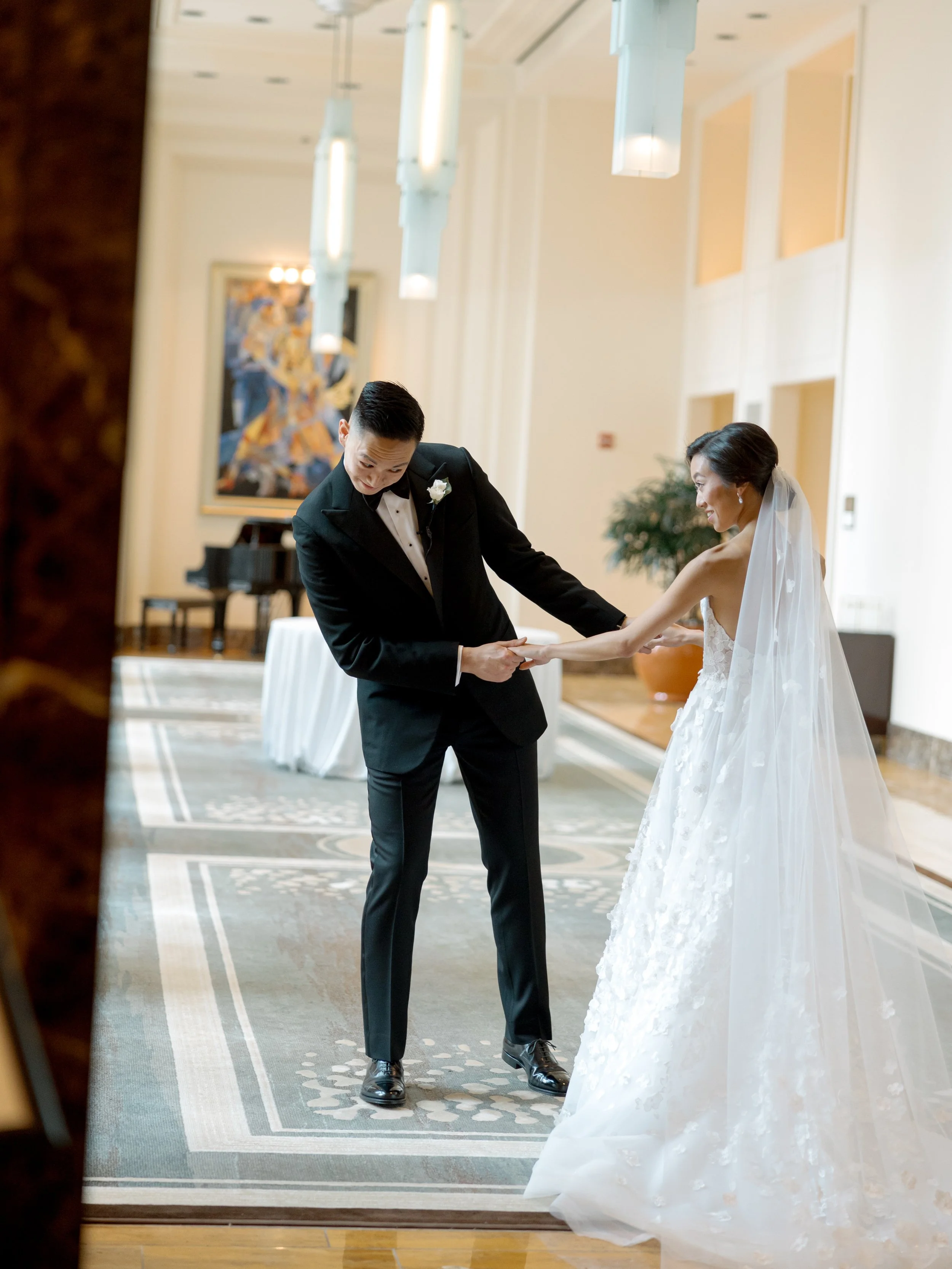Film first look photograph of the bride and groom holding hands in the Peninsula Chicago lobby near the grand piano