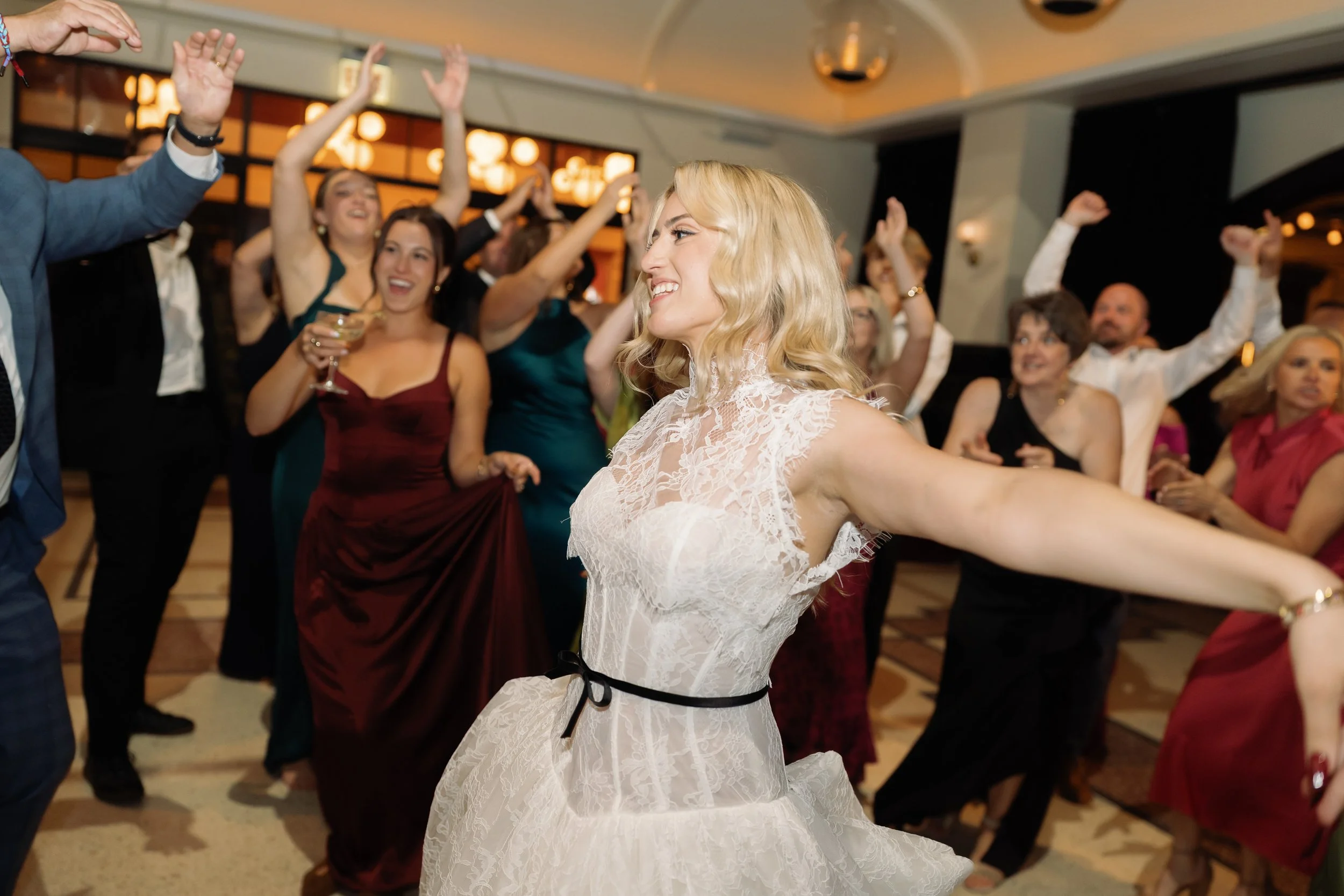 Bride dances with arms outstretched as guests cheer around her on the dance floor