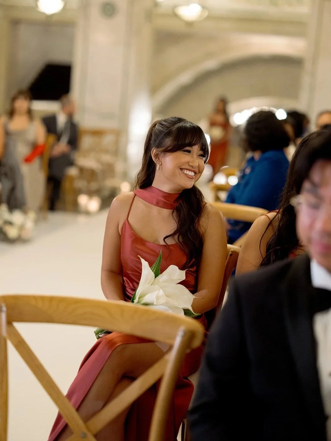 A wedding guest in a burgundy dress waiting for the bride to walk down the aisle