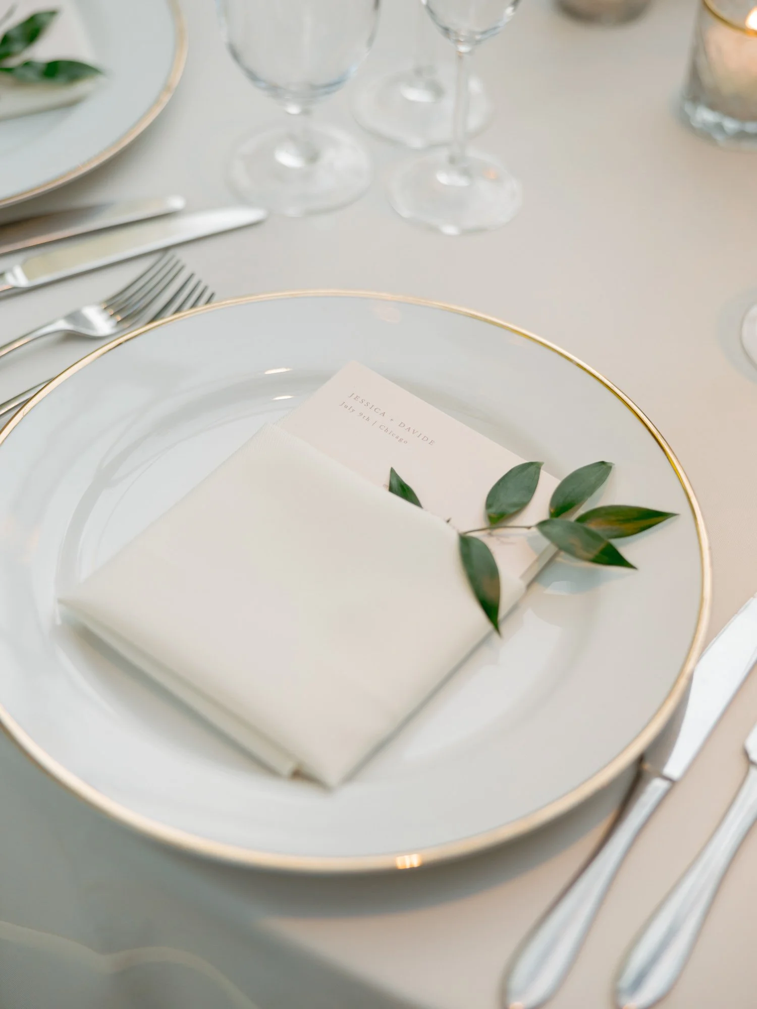 An exquisite reception place setting at the Chicago Illuminating Company: a gold-rimmed white charger, neatly folded napkin, menu card, and fresh eucalyptus sprig.