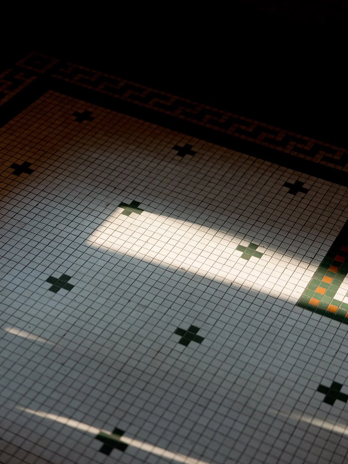Cafe Brauer's original Arts and Crafts mosaic tile floor with a shaft of sunlight casting a soft rectangle across its surface.