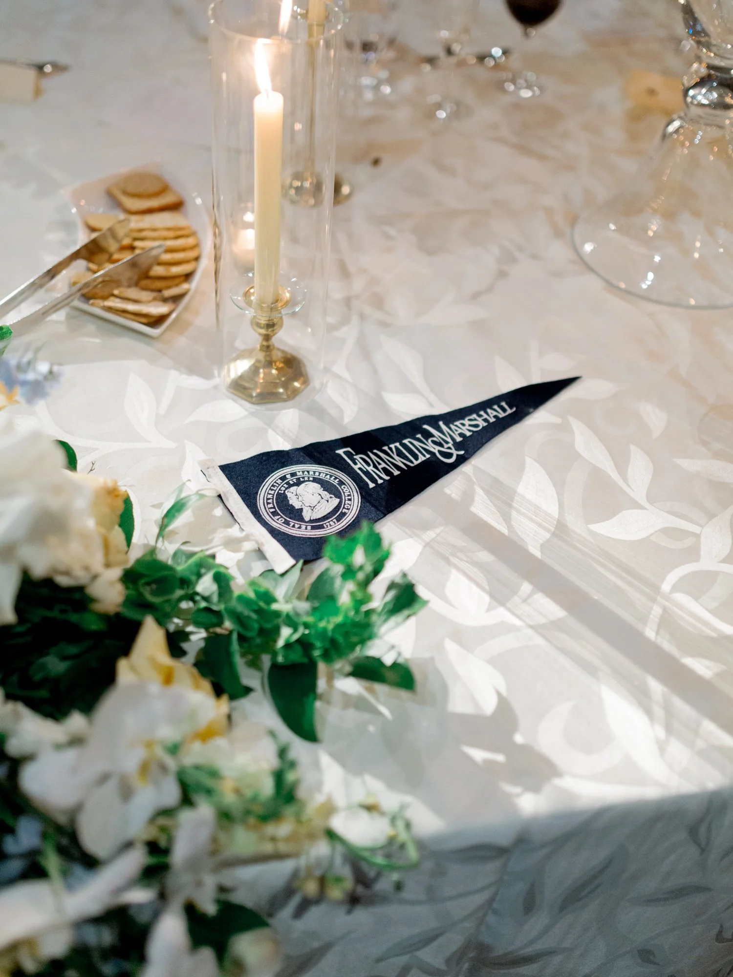 A Franklin and Marshall pennant tucks into the floral centerpiece beside a taper candle — personal, specific, and exactly the kind of detail that matters.
