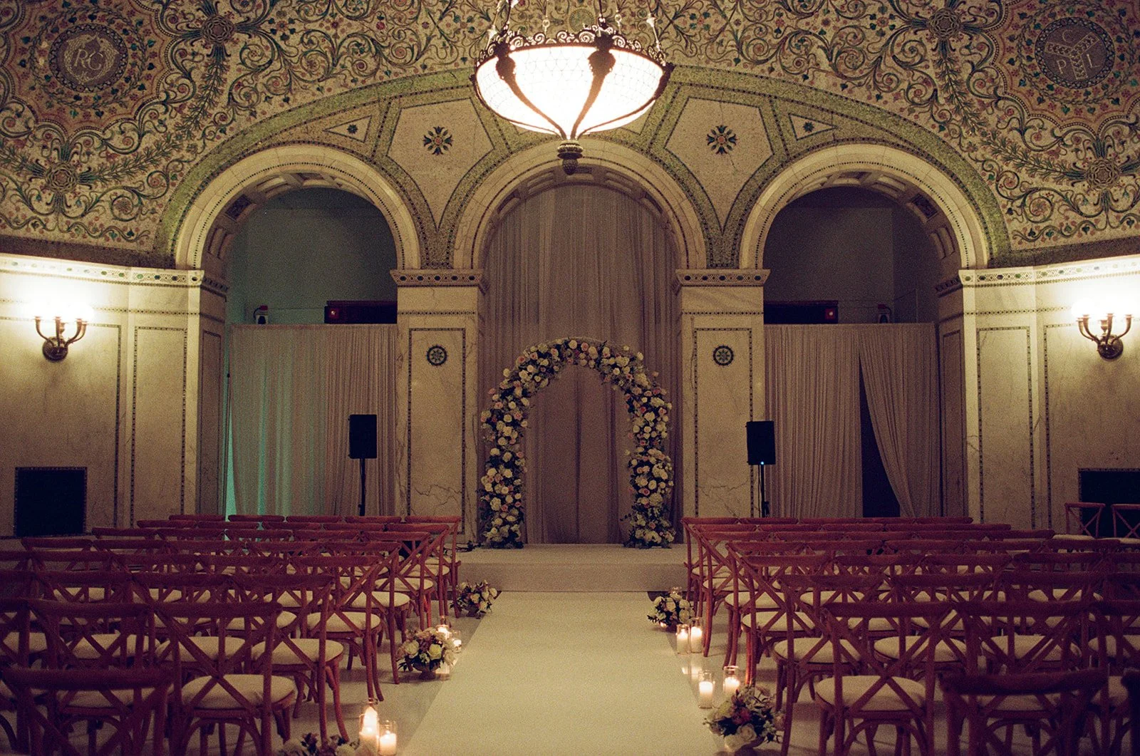Ceremony setup in the stunning Preston Bradley Hall at Chicago Cultural Center, featuring an elegant white floral arch framed by ornate architecture and warm lighting. Shot on film by a Chicago film wedding photographer.