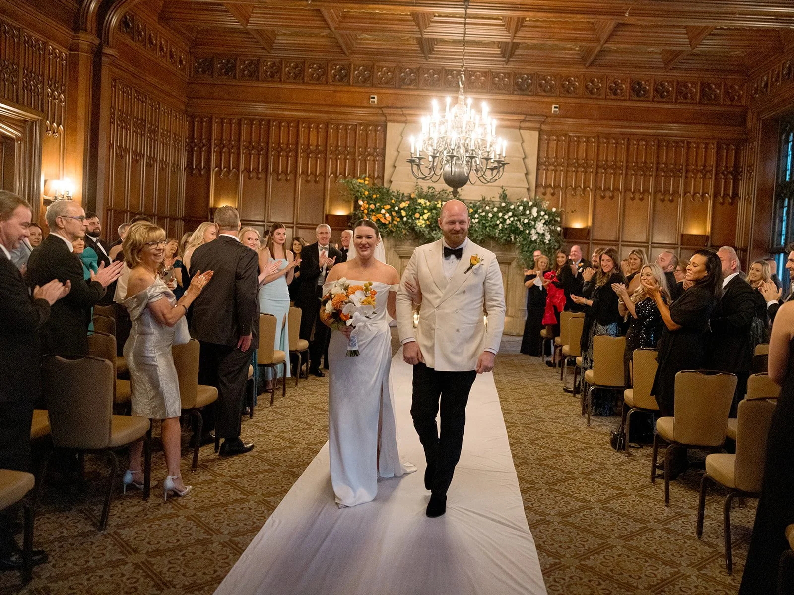 Couple walks back down aisle as newlyweds, guests applauding as they beam.