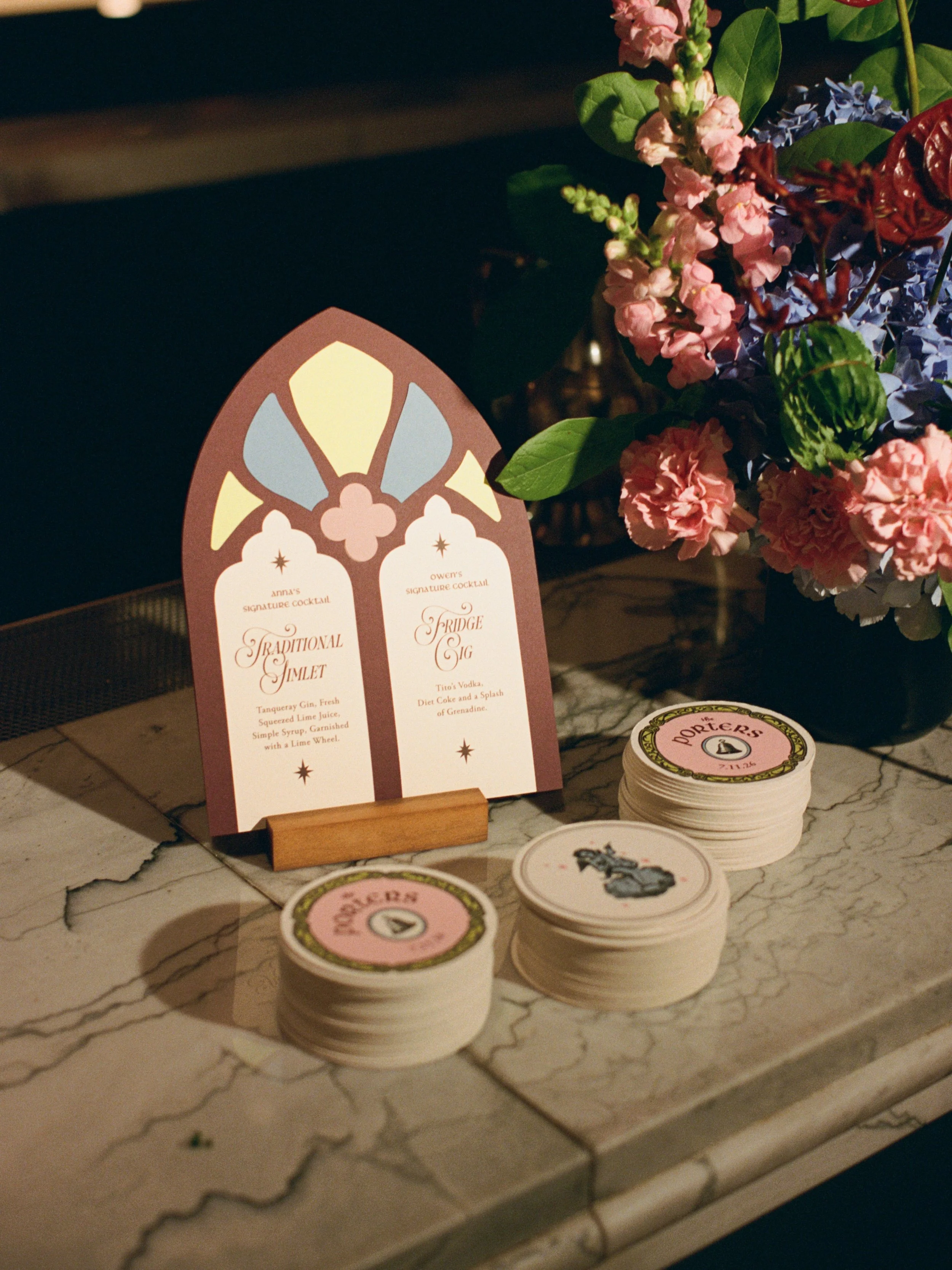 Stained glass inspired escort cards and wax seal coasters displayed on a marble ledge with florals