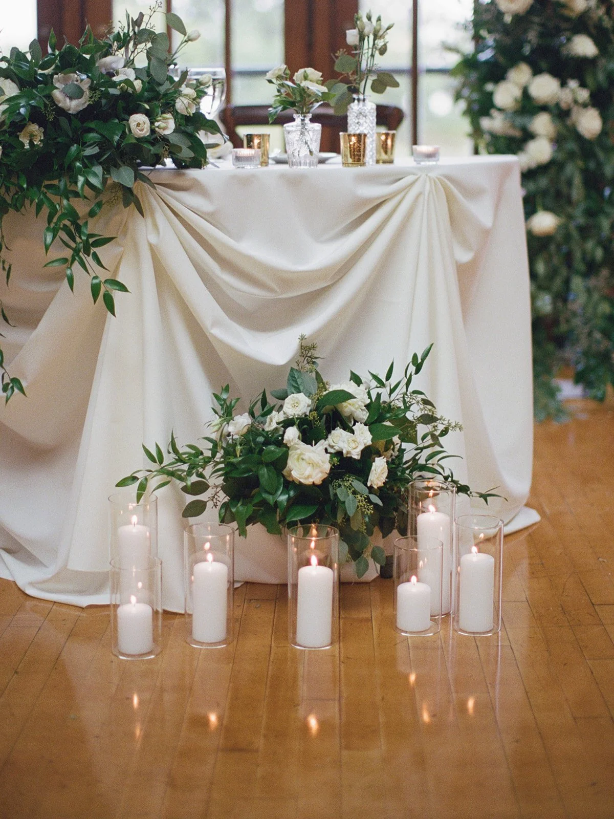 Close detail of the sweetheart table base at Cafe Brauer — pillar candles around a white peonies and eucalyptus arrangement.