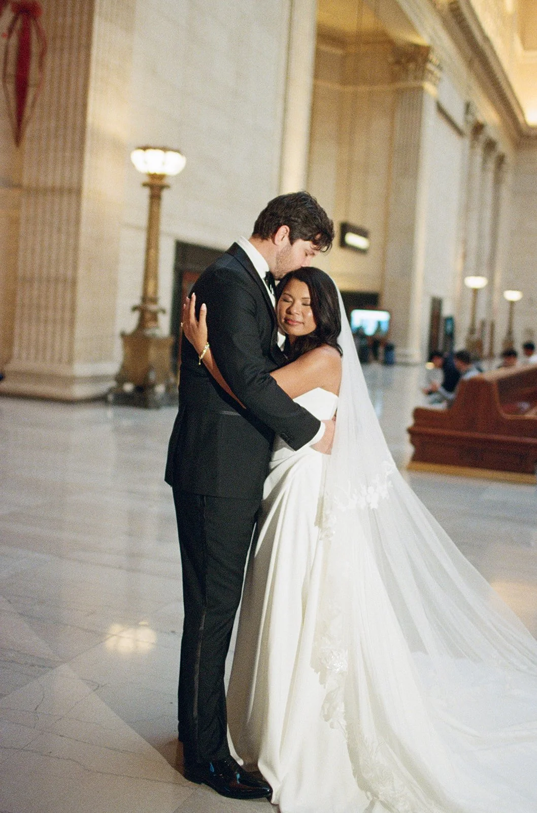 Sarah and Brennan embrace in Chicago Cultural Center's elegant marble hall with classical columns. Shot on film by a Chicago film wedding photographer.