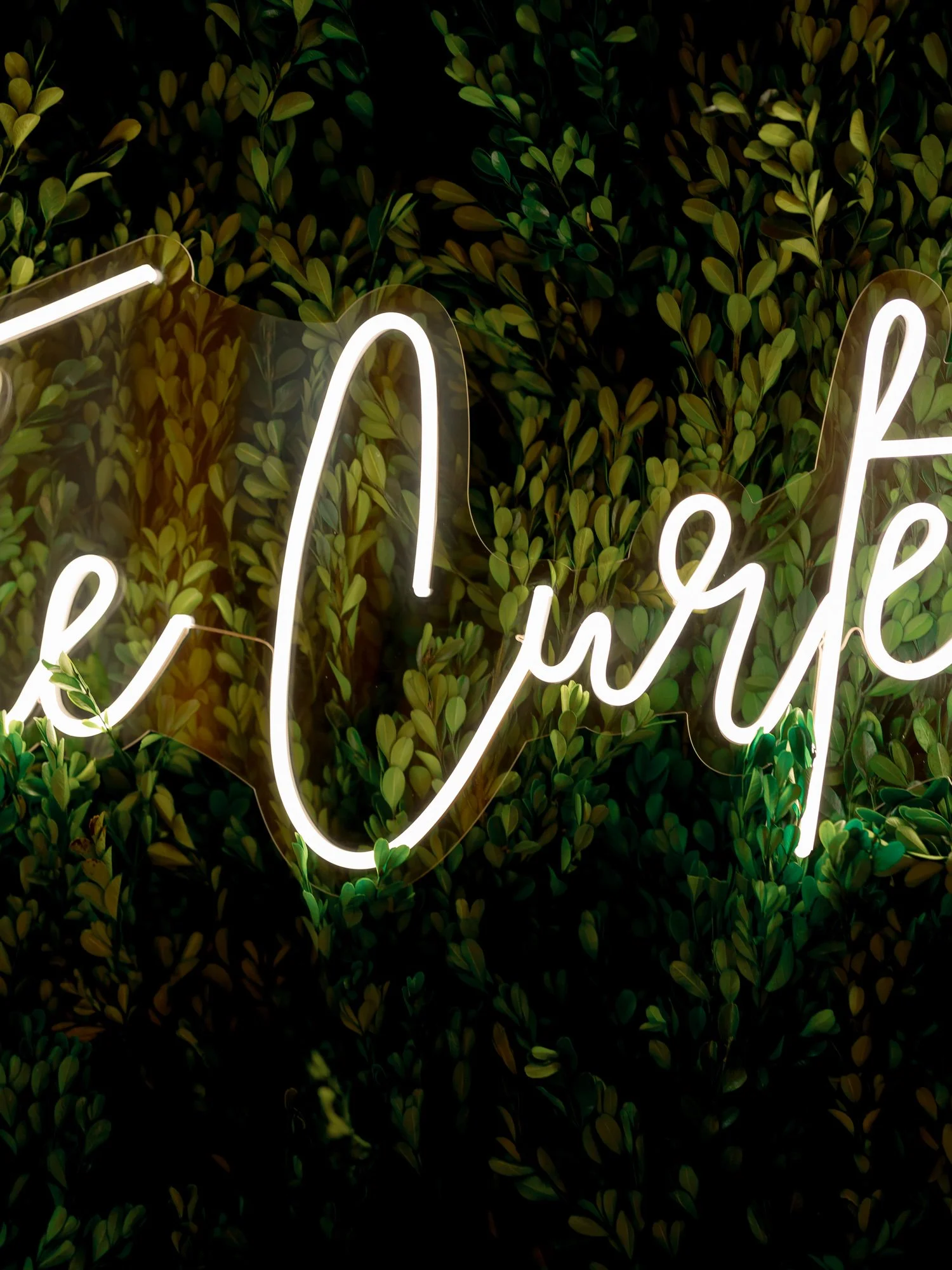 A glowing white neon sign spelling the couple's surname illuminates a lush green boxwood wall at the Chicago Illuminating Company wedding reception.