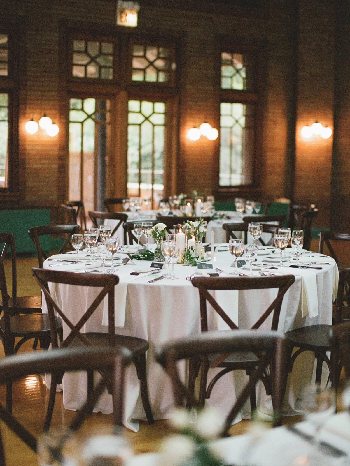 Cafe Brauer reception room set with round tables in white linens, dark wood cross-back chairs, and warm globe sconces.