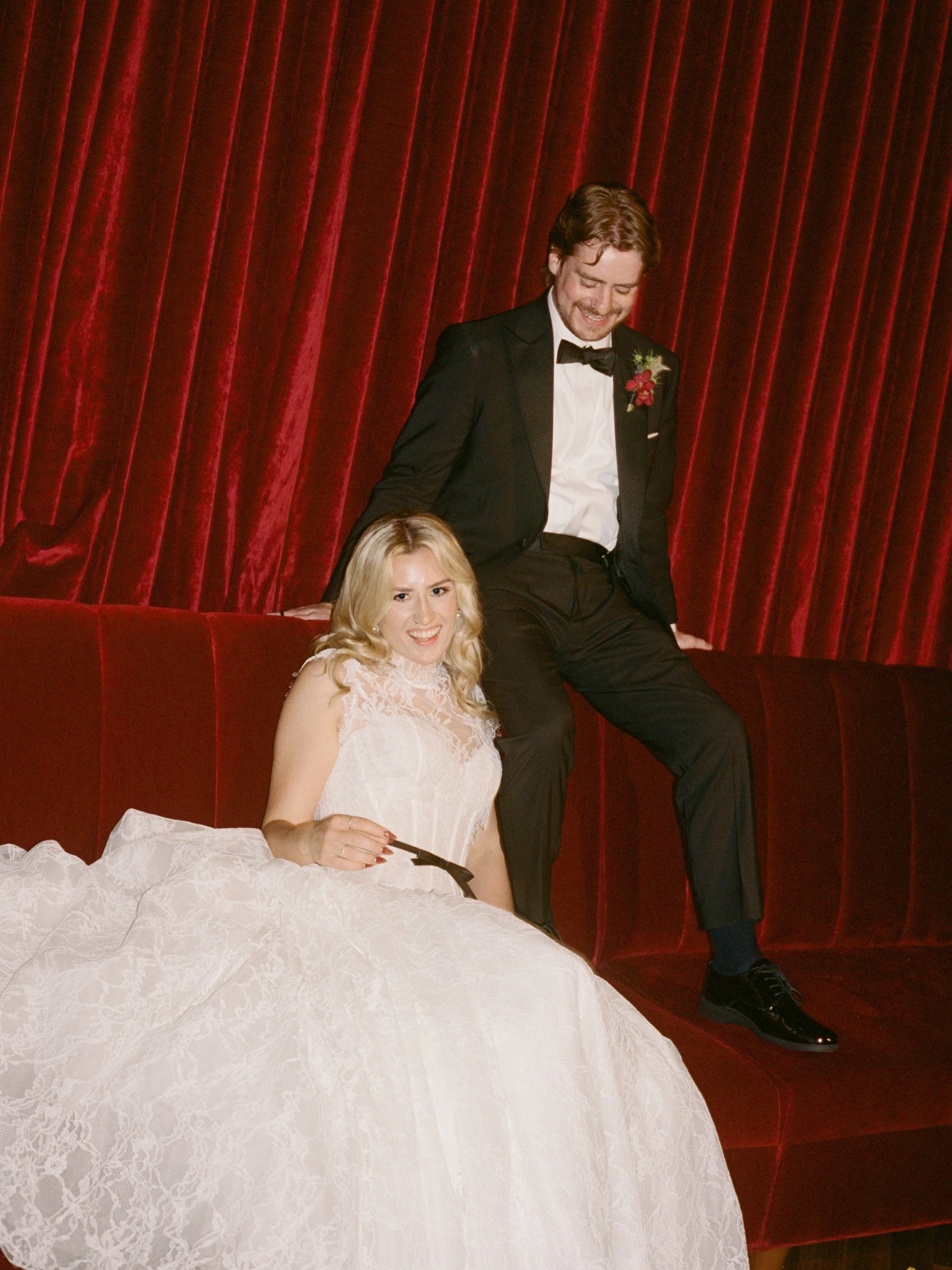 Bride sits on a velvet couch in The Wellsley's red velvet lounge while the groom leans on the backrest behind her