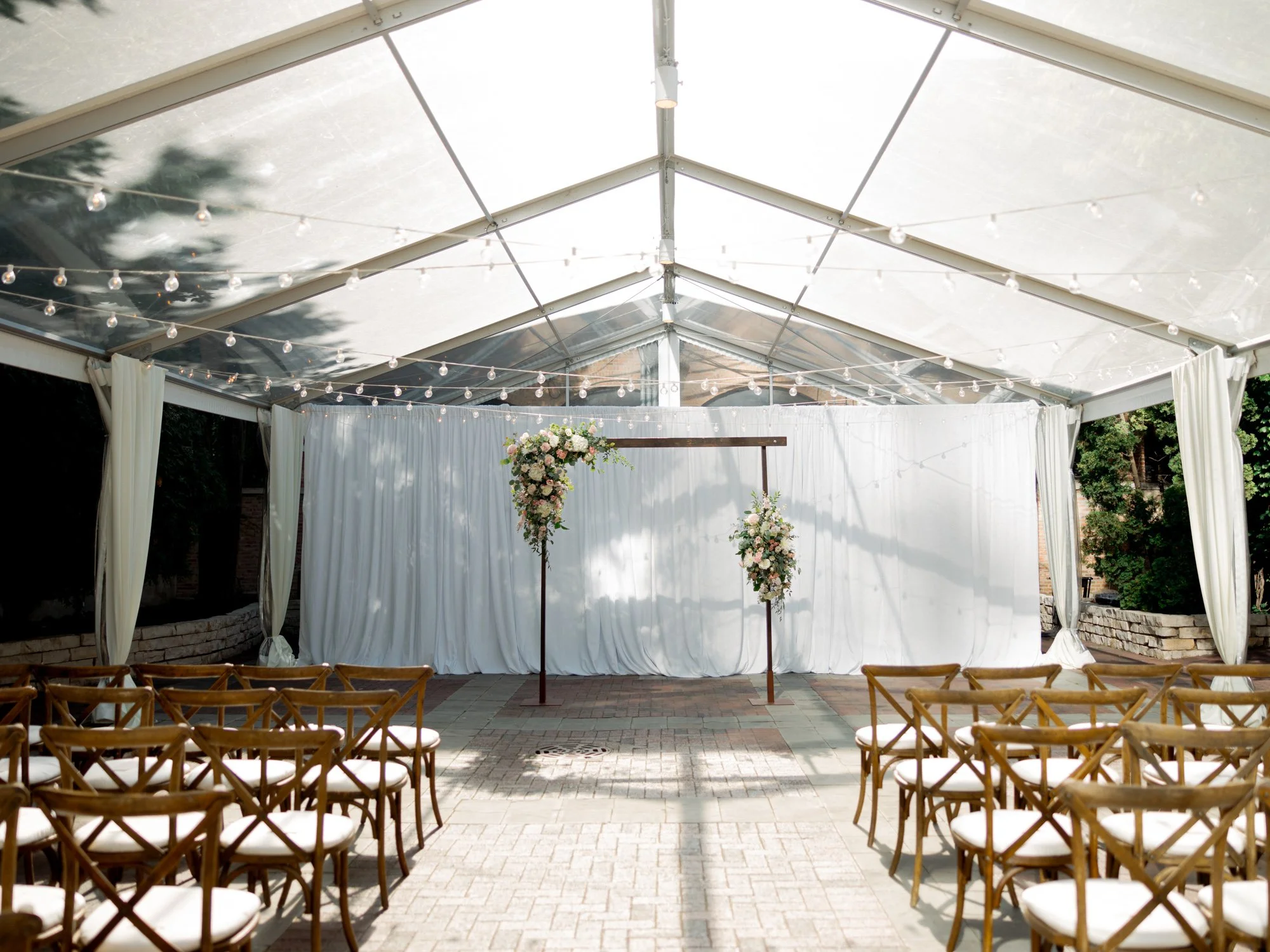 The Chicago Illuminating Company ceremony space before guests arrive, wooden chairs in crisp rows and a floral arch framed by white draping and the glass roof.