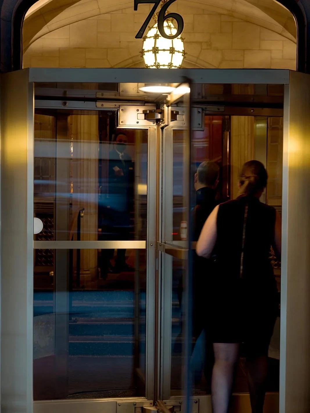A woman in black disappears through the University Club Chicago's glowing gold revolving door at night — a moody, street-level exterior shot that feels more like a film still than a wedding photo. Shot on film by a Chicago film wedding photographer.