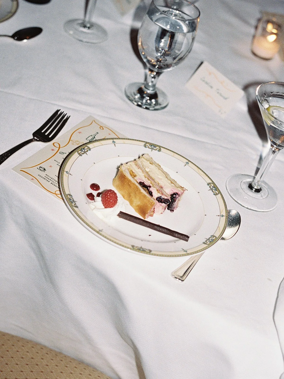 A slice of wedding cake on monogrammed University Club china — berry and cream filling, the illustrated menu card still tucked beside the plate. An end-of-dinner detail that feels quietly perfect — by a Chicago film wedding photographer.