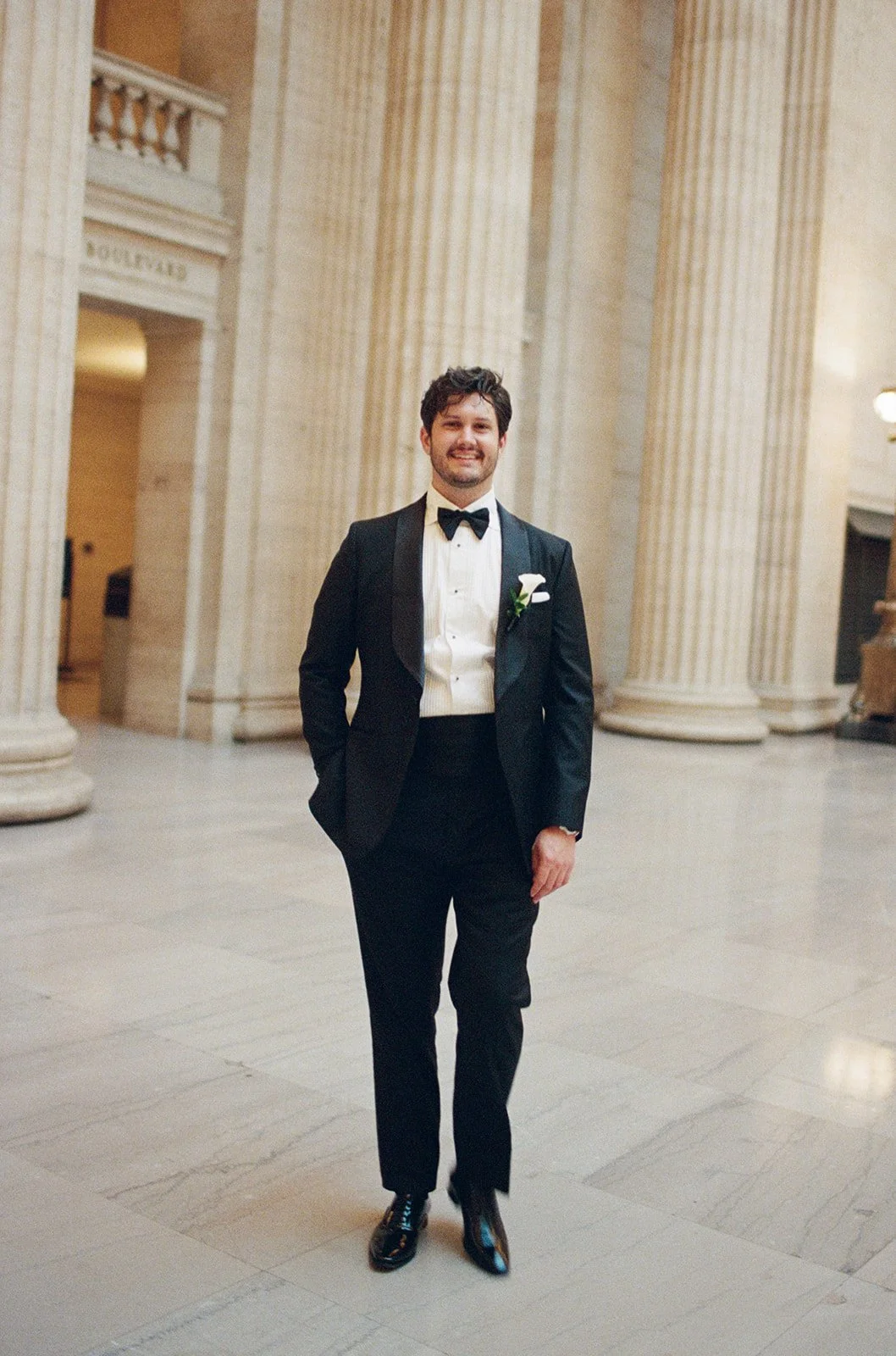 Brennan in his black tuxedo and crisp white shirt, posed among the classical columns of Chicago Cultural Center. Shot on film by a Chicago film wedding photographer.