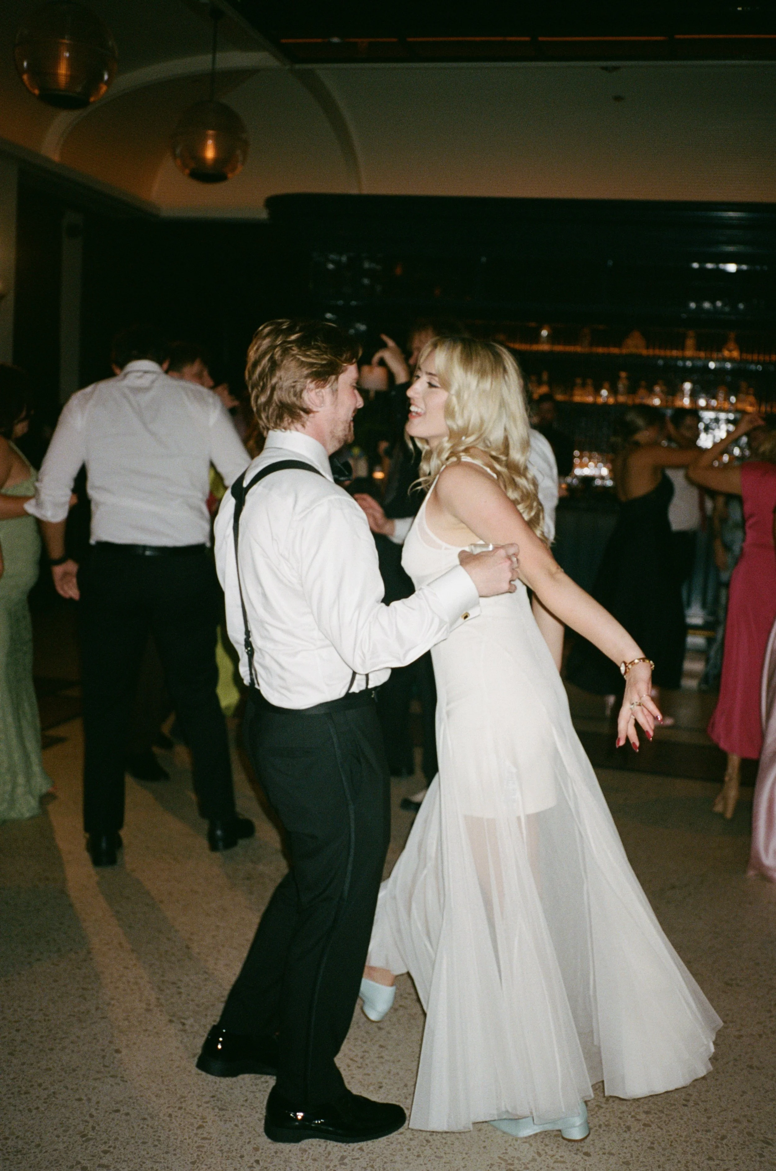 Bride and groom dance together at the reception with the bar glowing behind them