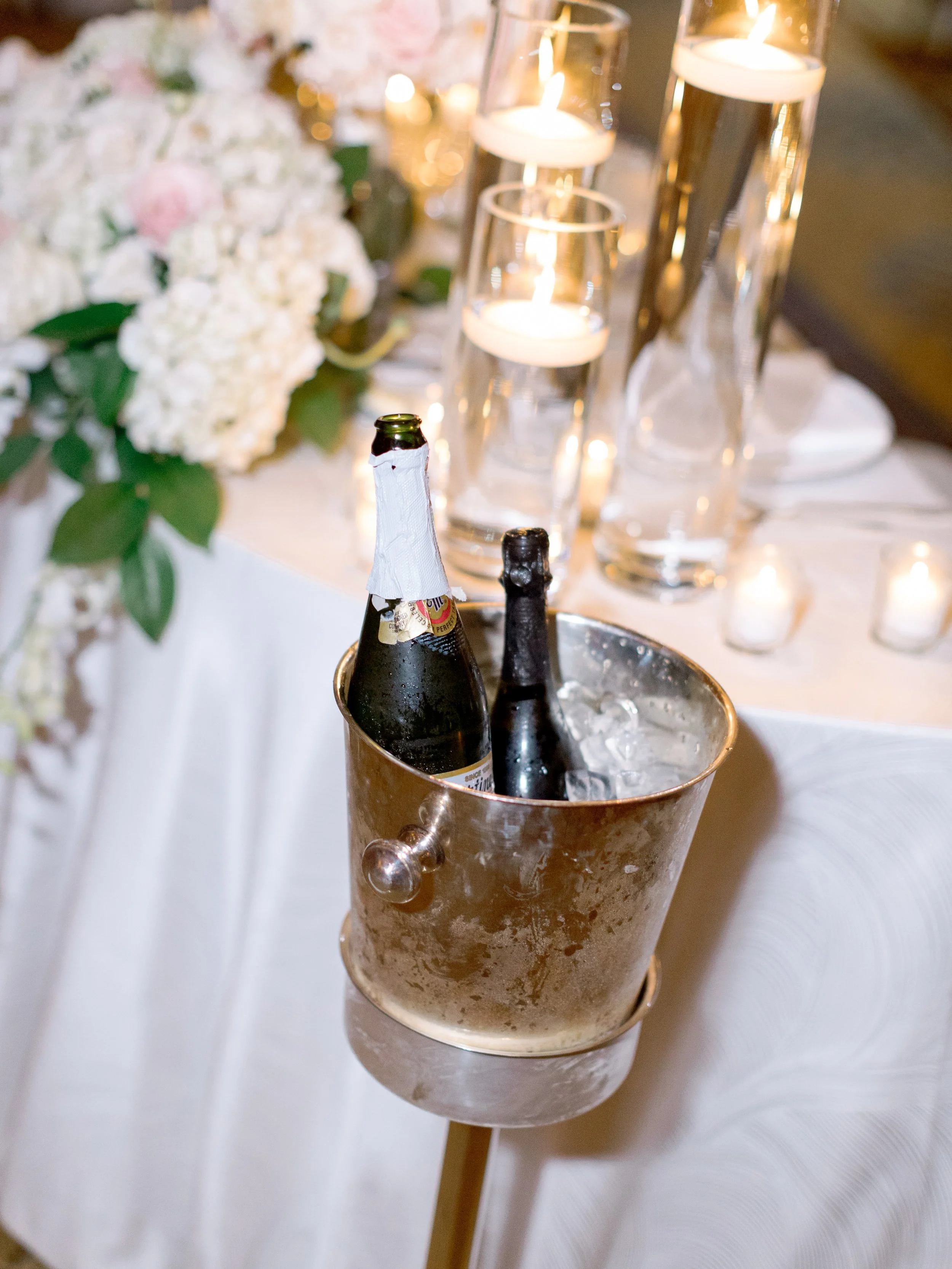 Gold champagne bucket with Moet bottles beside floating candles and blush rose centerpiece at Peninsula Hotel Chicago wedding