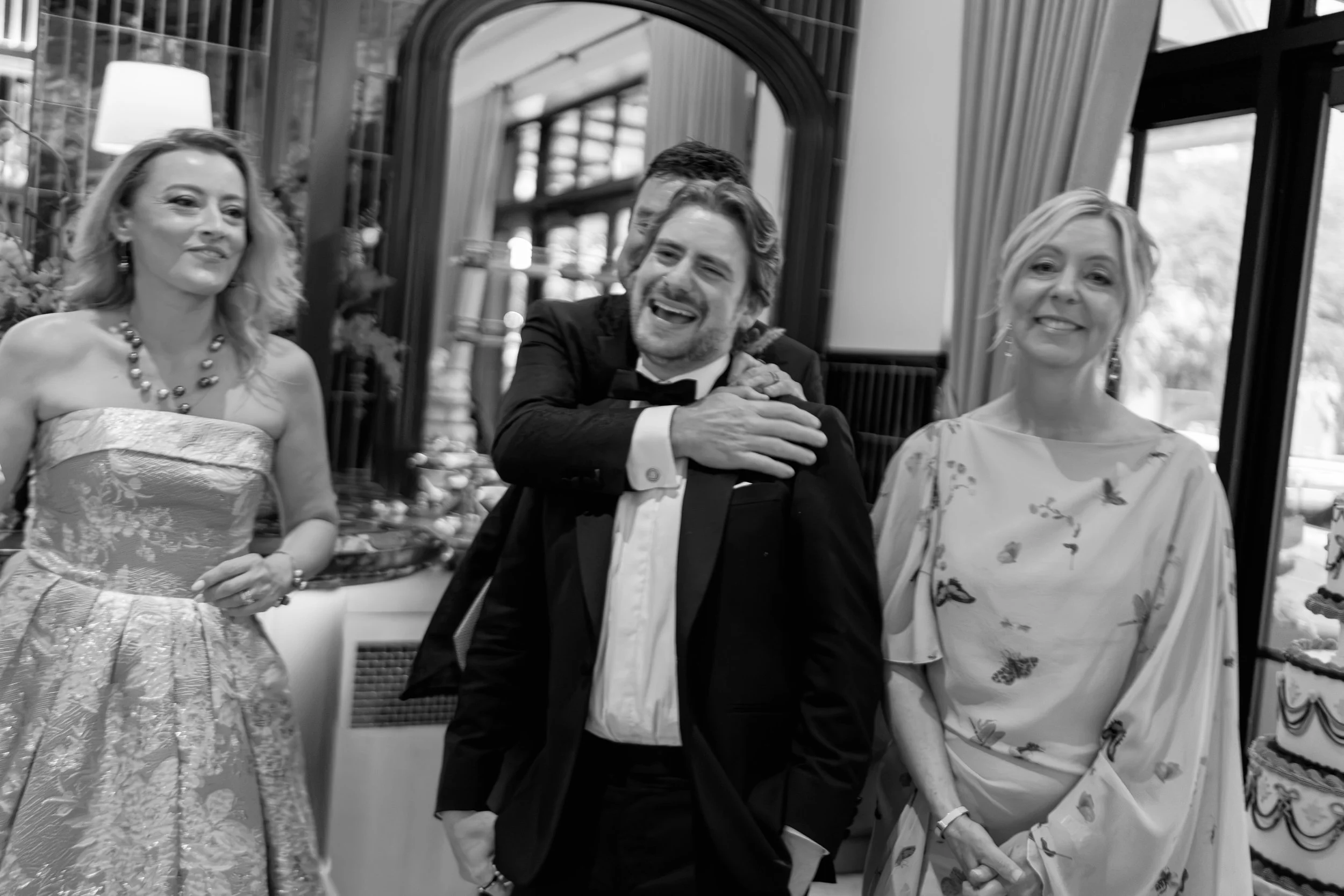 Black and white candid of guests laughing together near a mirrored bar