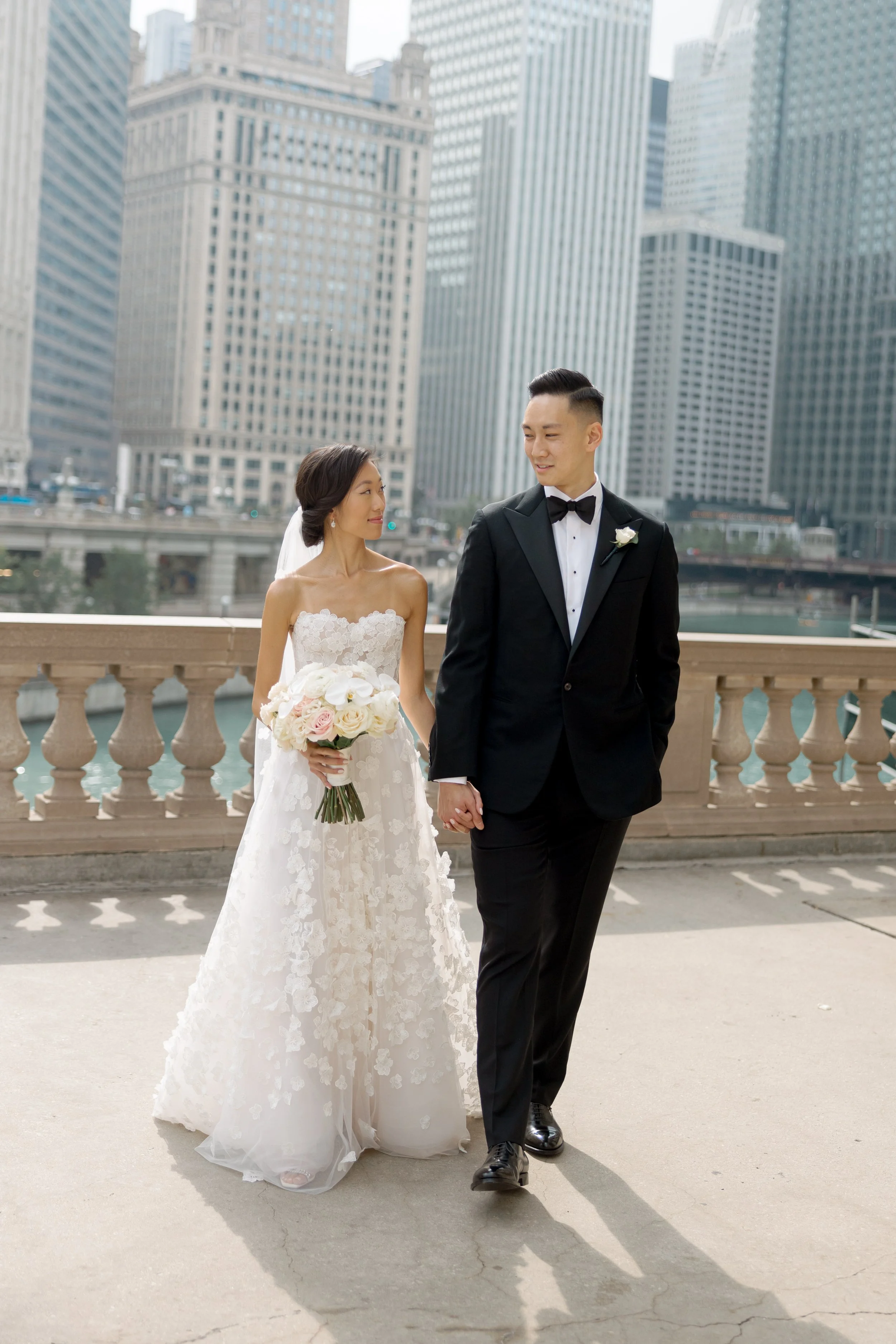 Film photograph of the bride and groom walking hand in hand across a Chicago River bridge with downtown skyscrapers behind