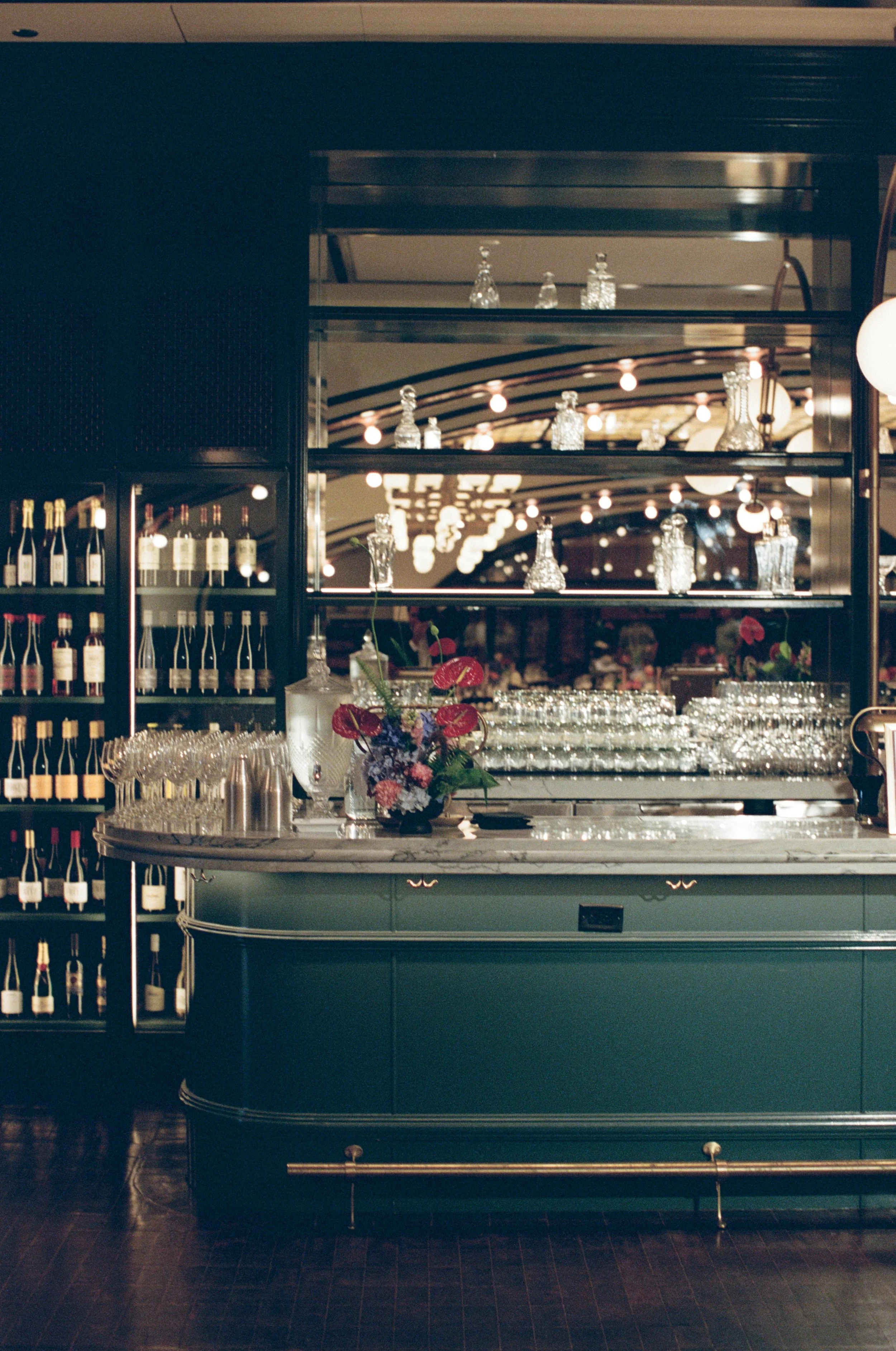 Moody emerald green bar with mirrored shelves, wine glasses, and a fresh floral arrangement at The Wellsley